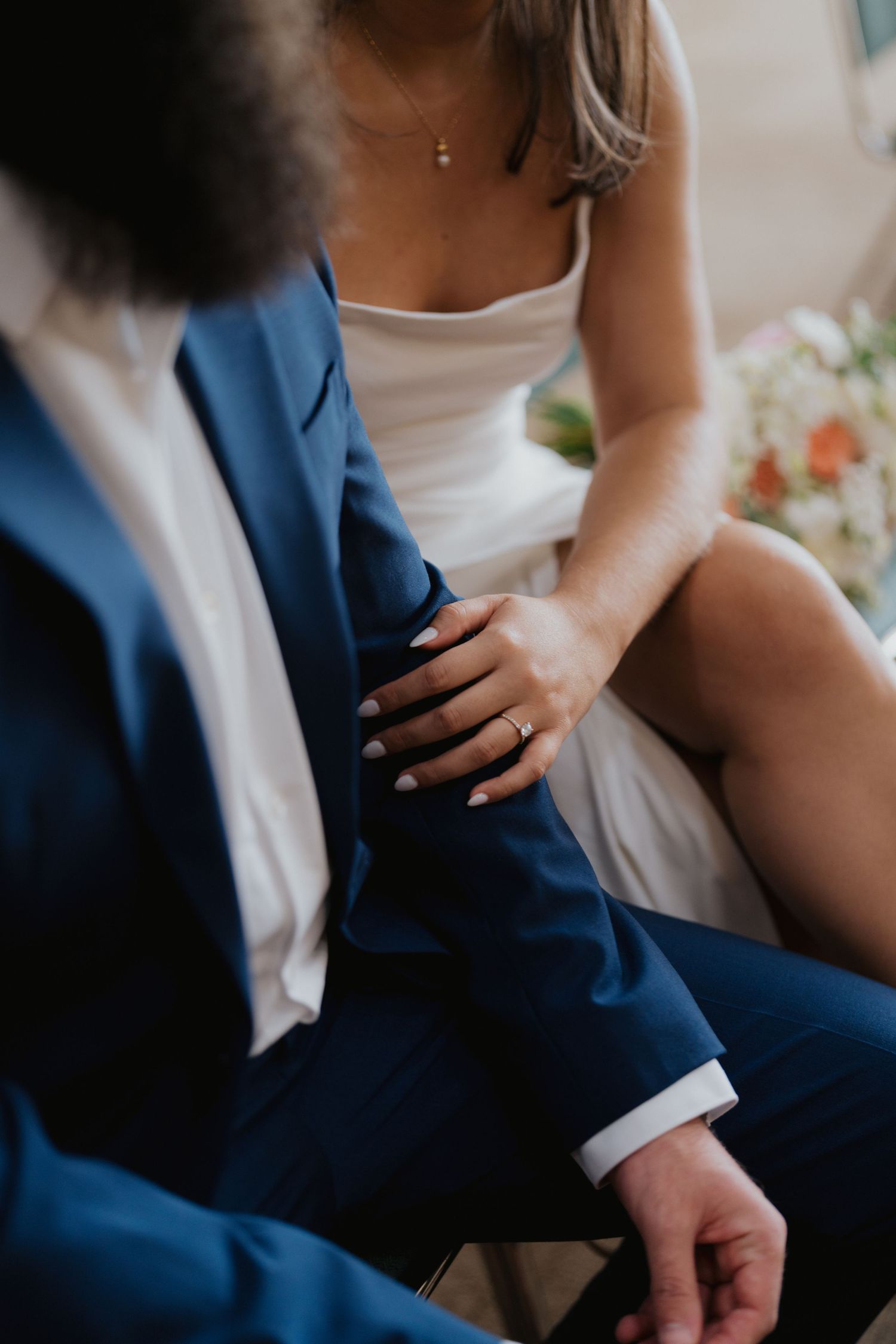 Close-up shot of two people sitting together with focus on formal attire and clasped hands.
