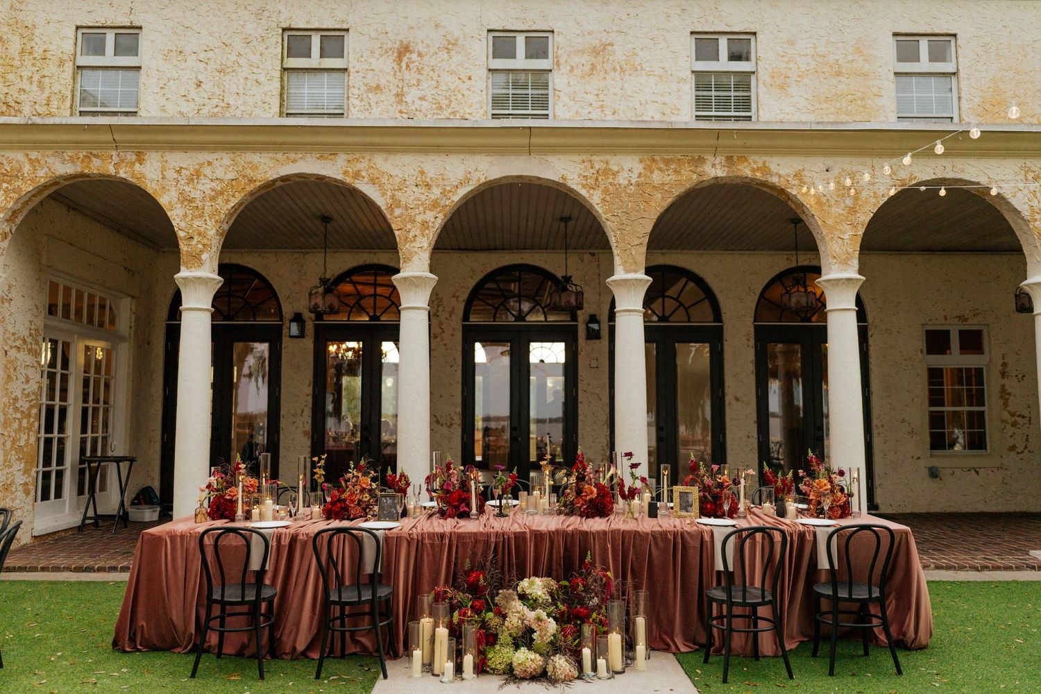 Tables and chairs set up for an elegant outdoor wedding reception under stone archways and columns.