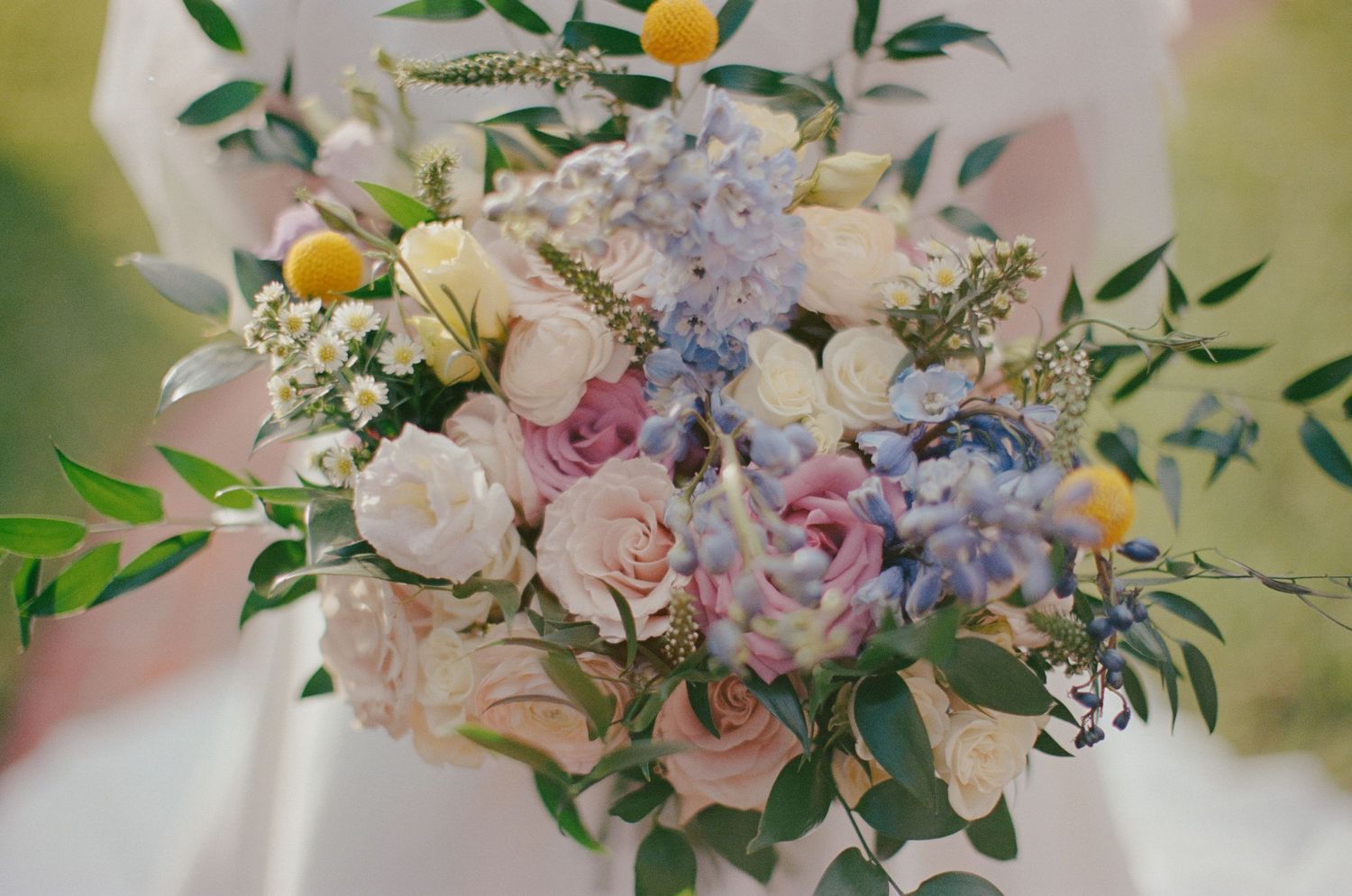 Elegant bridal bouquet featuring pastel pink roses, blue hydrangeas, white blooms, and lemon accents with lush greenery.