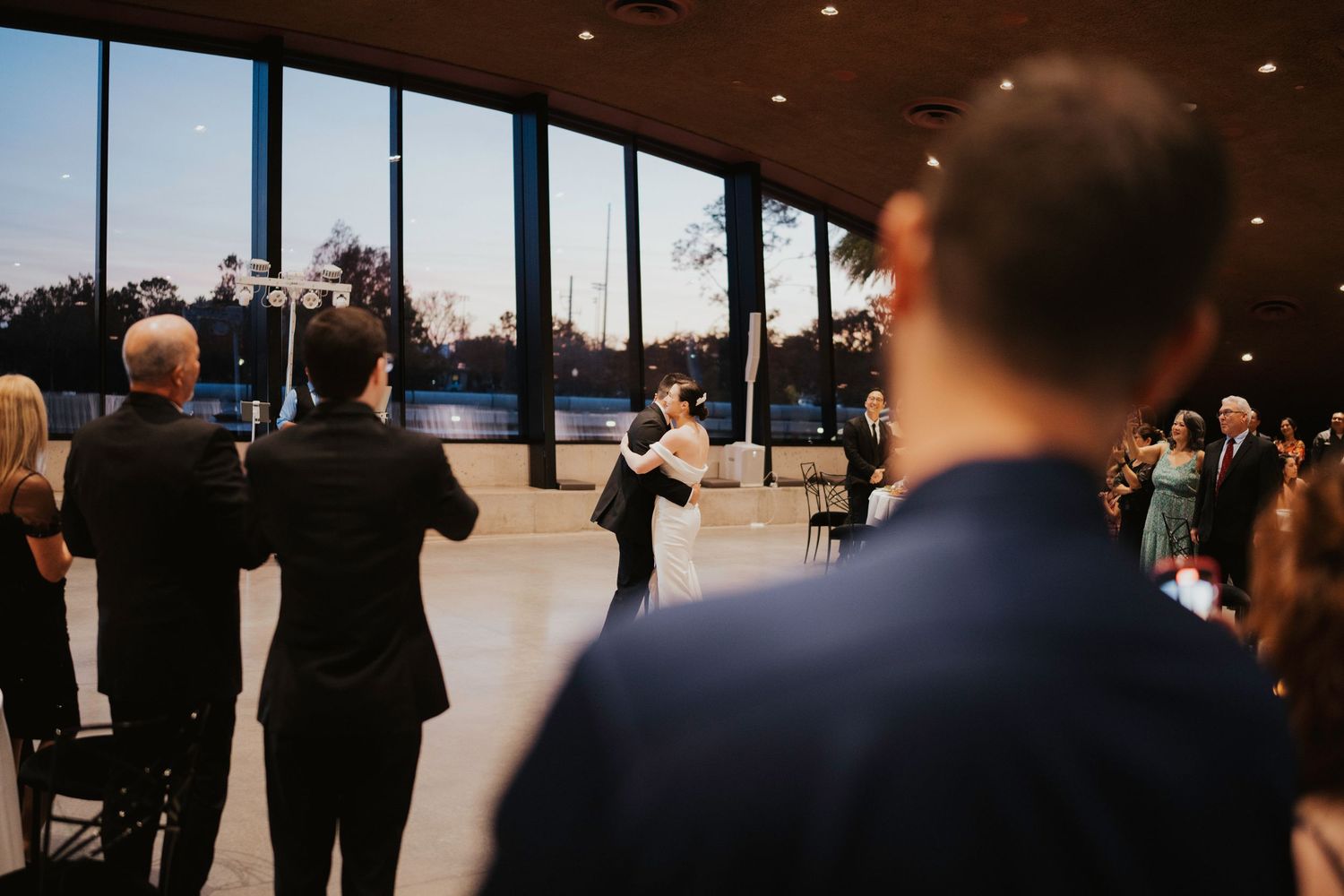 Wide angle view of wedding guests seated in rows at an indoor ceremony space.