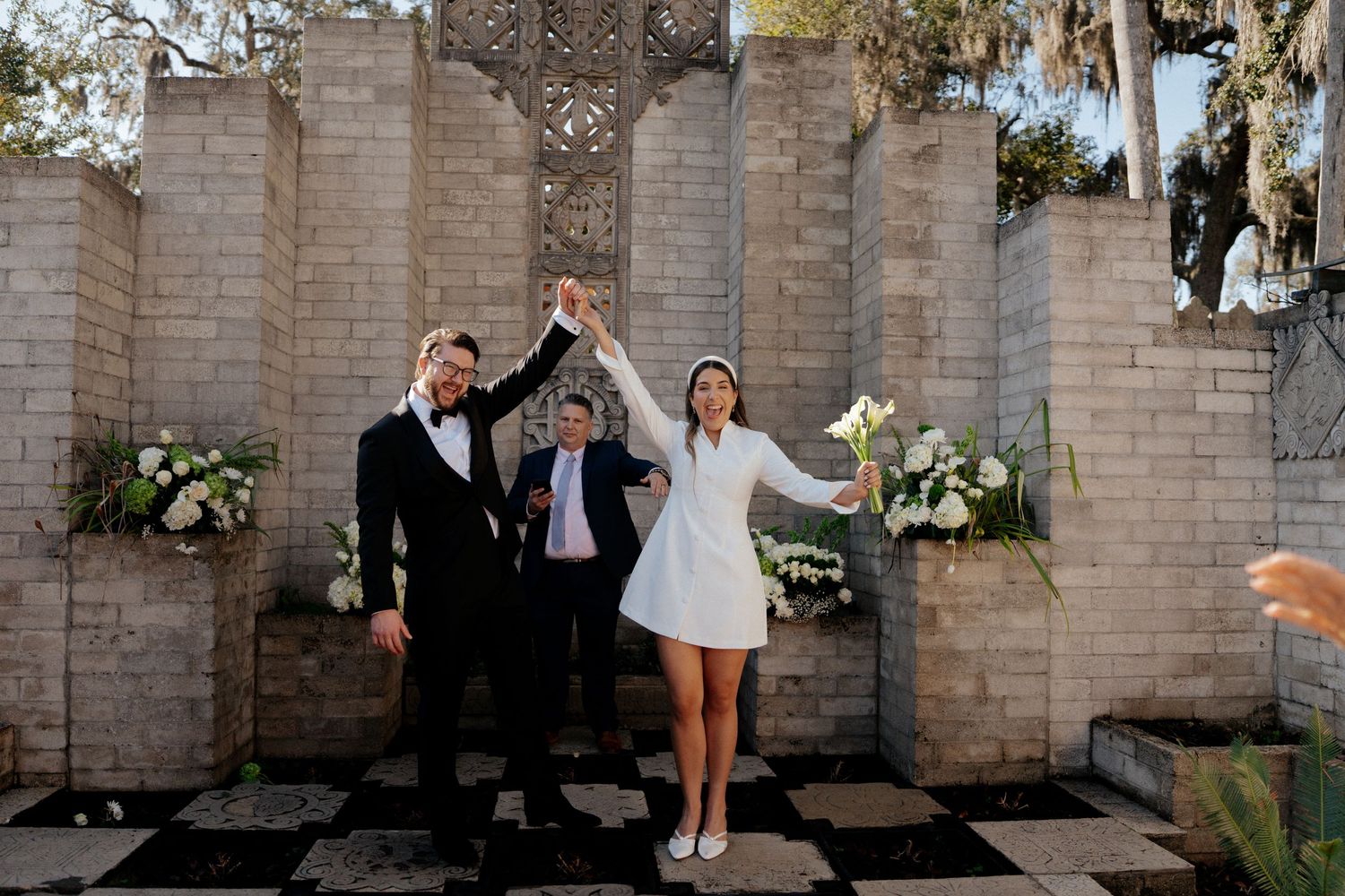 A celebratory moment at an outdoor wedding ceremony with stone walls and floral decorations.