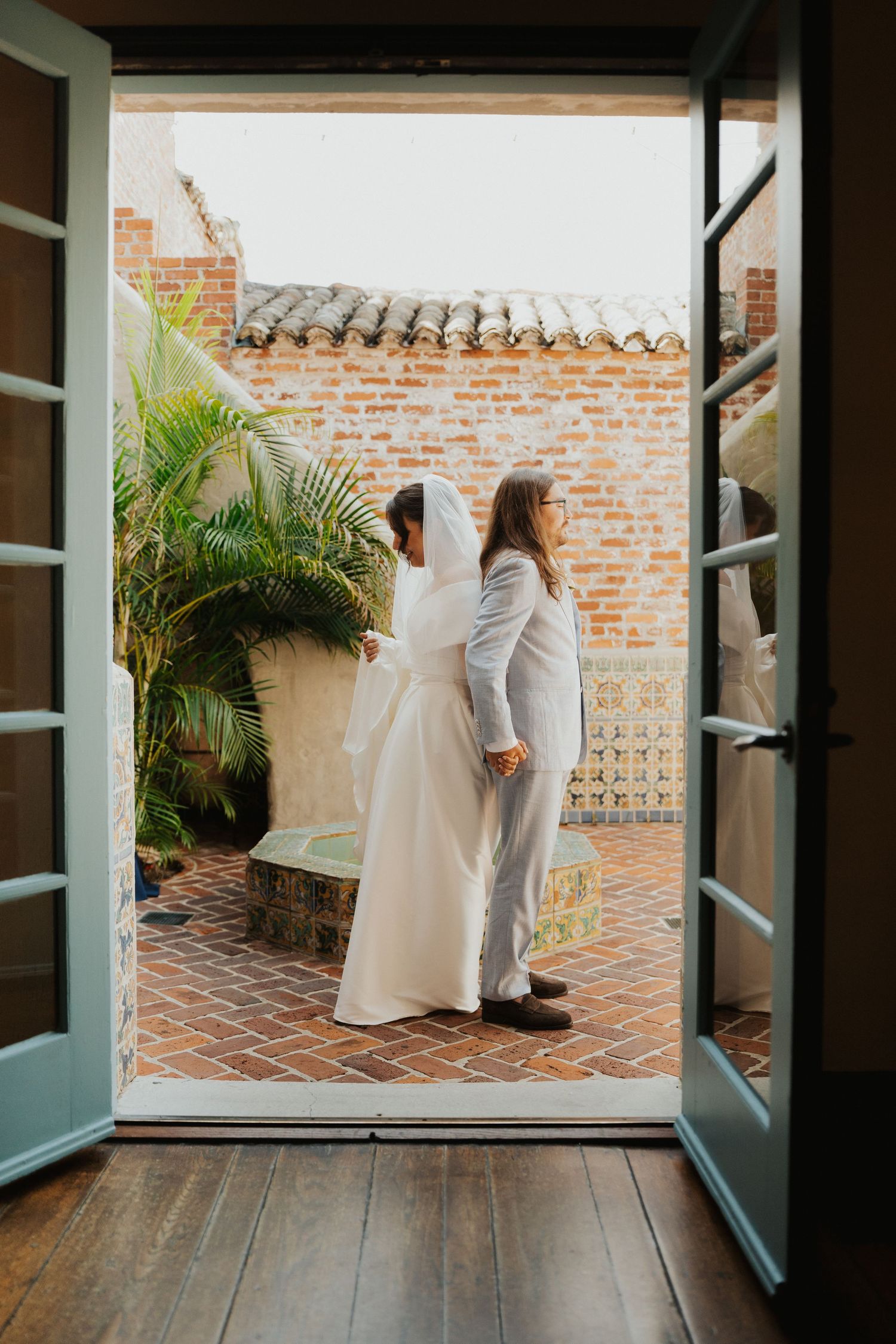 French doors open to a brick courtyard patio with palm trees and terra cotta tiles.