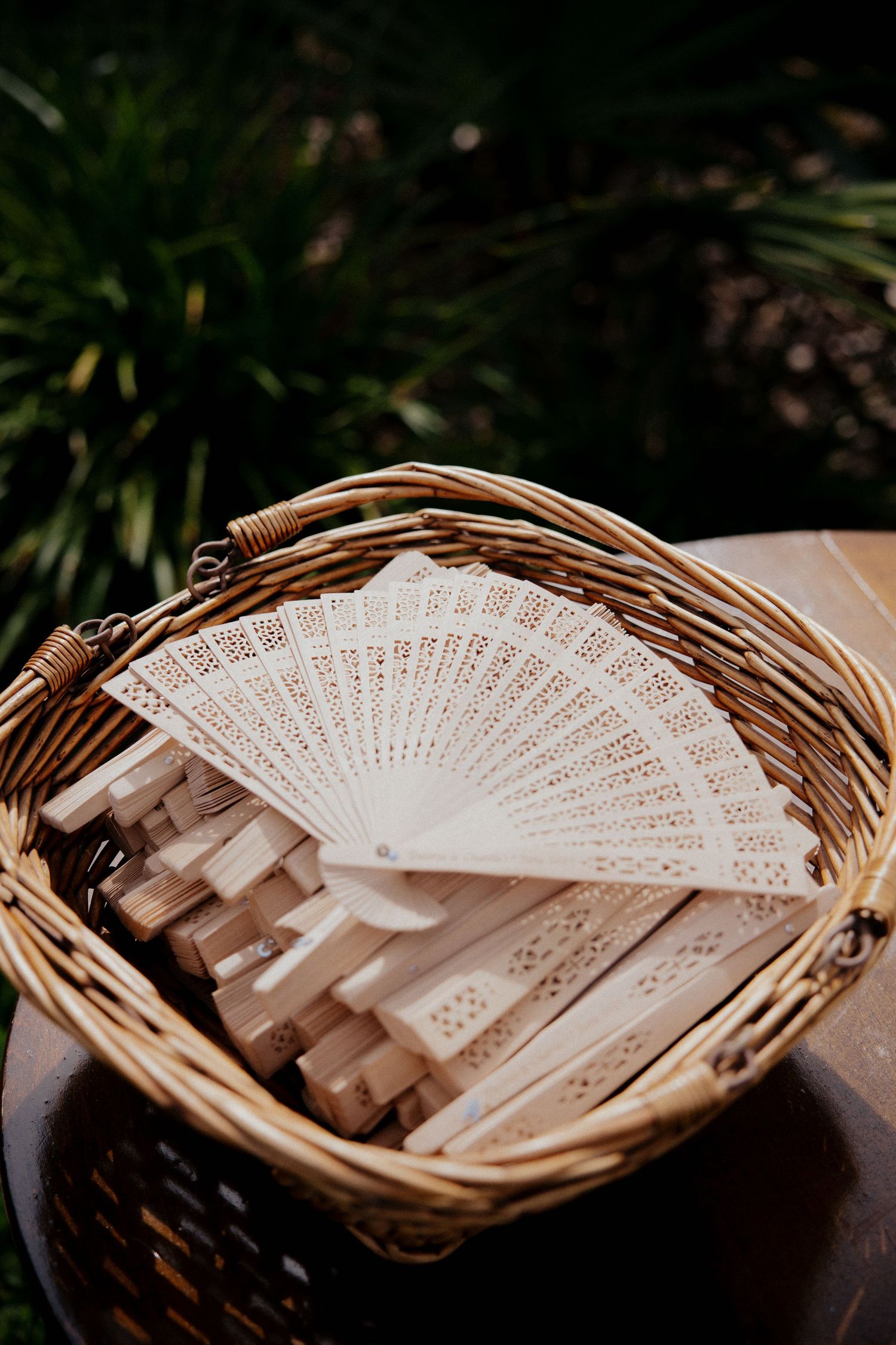 Decorative white folding fans arranged in a wicker basket for wedding guests.