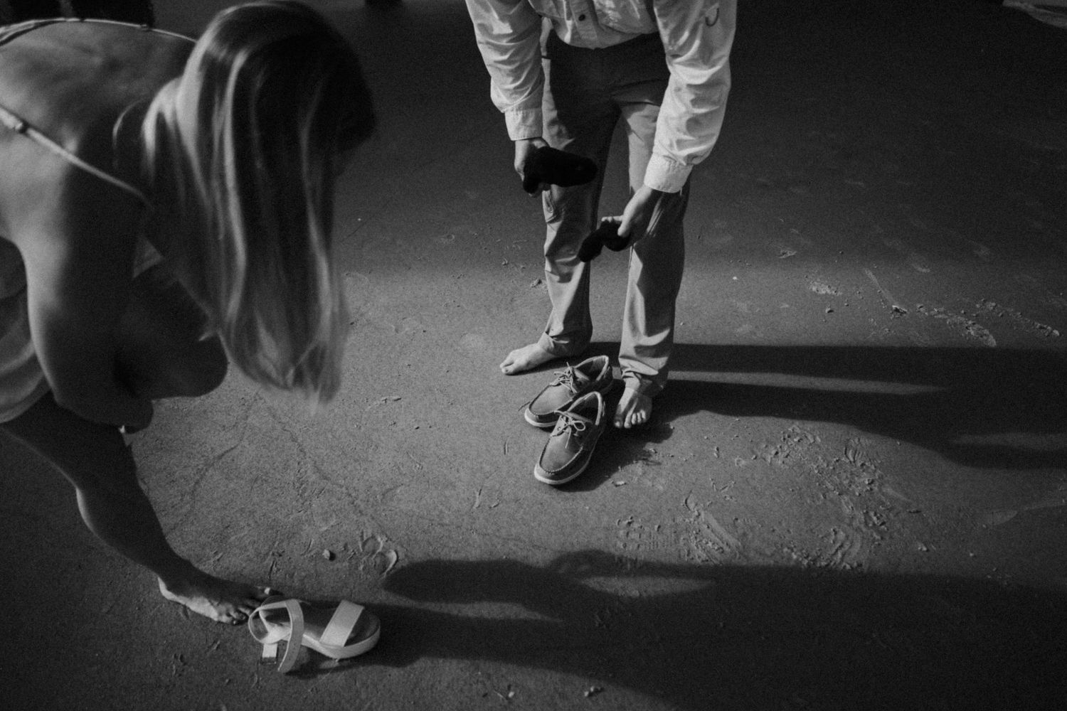 Black and white image of two people tying their shoes on a dark surface.