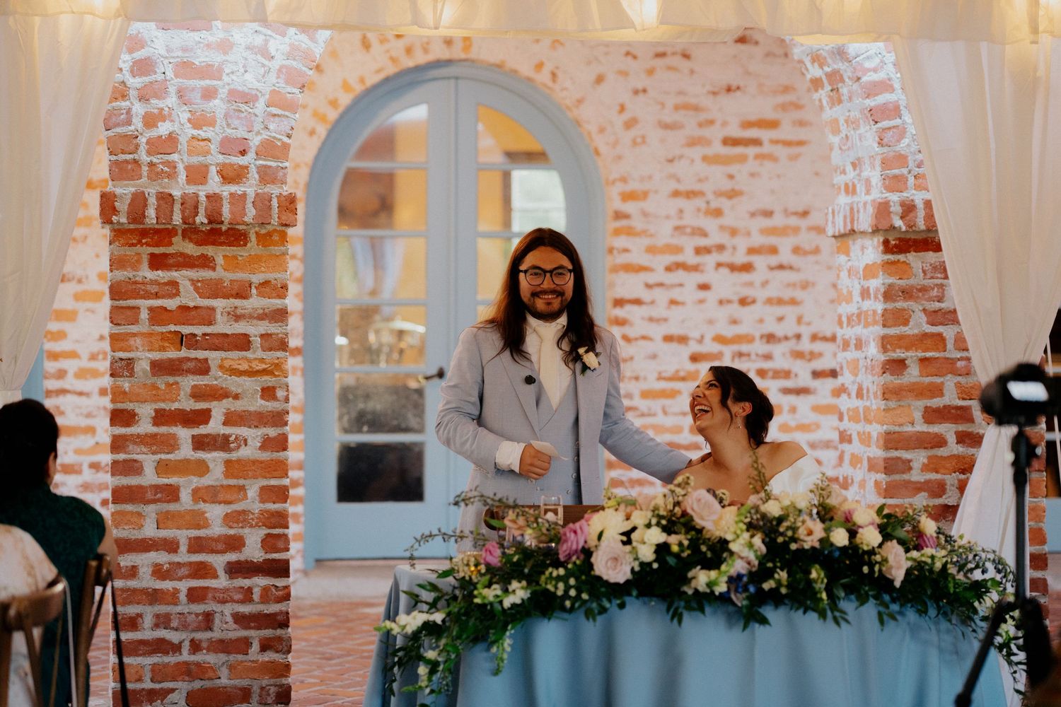 Wedding reception at a rustic brick venue with a light blue tablecloth and floral garland decorations.