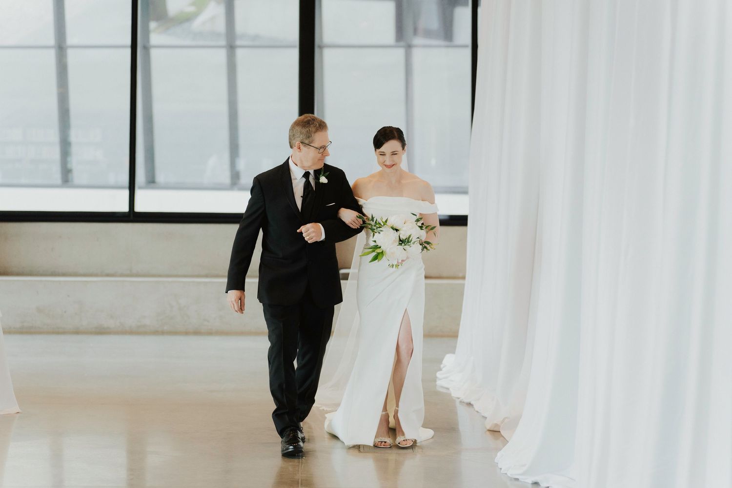 Elegant wedding ceremony setup in a modern space with white drapes and natural lighting.