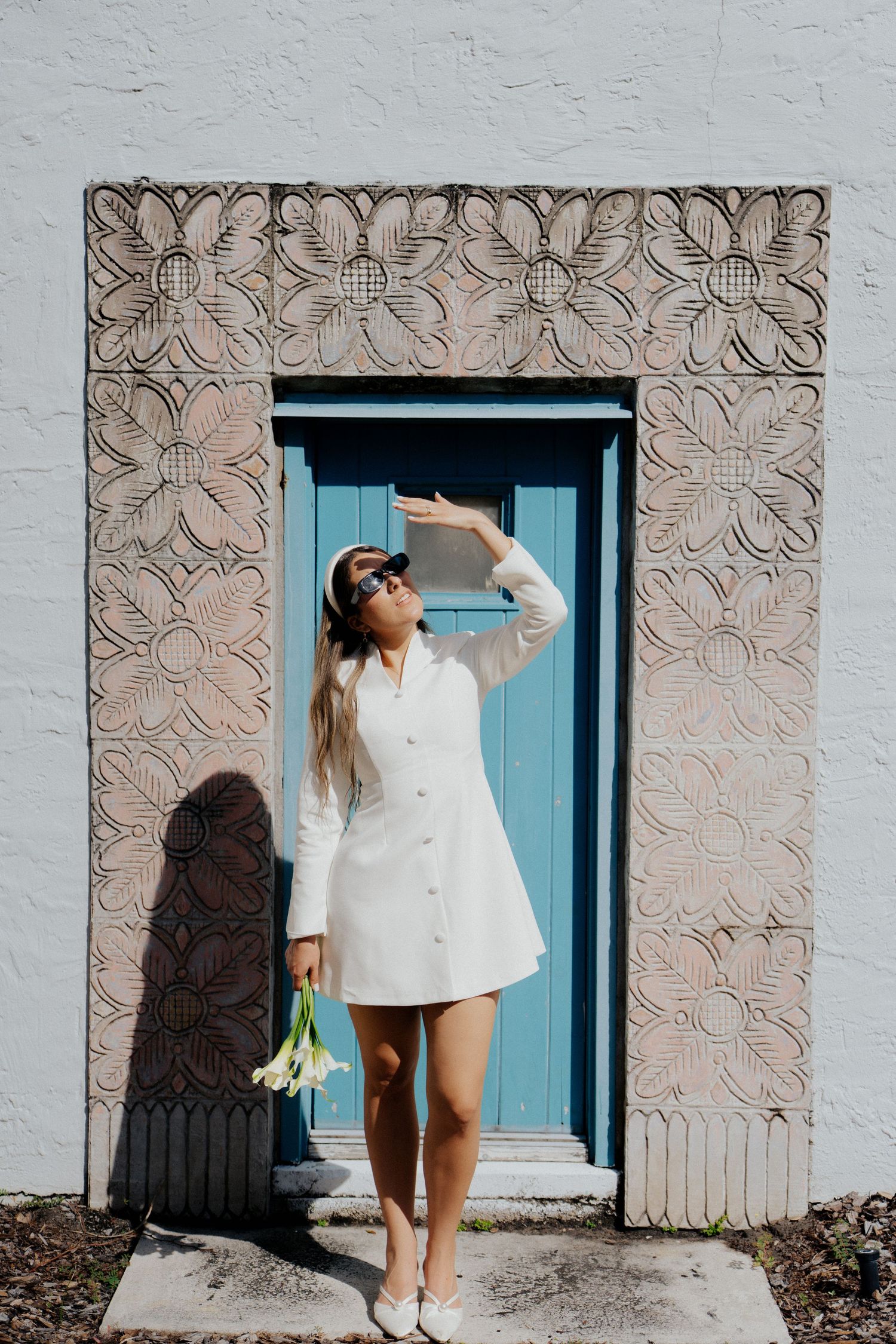 Woman in white dress posing against textured wall with turquoise blue door.
