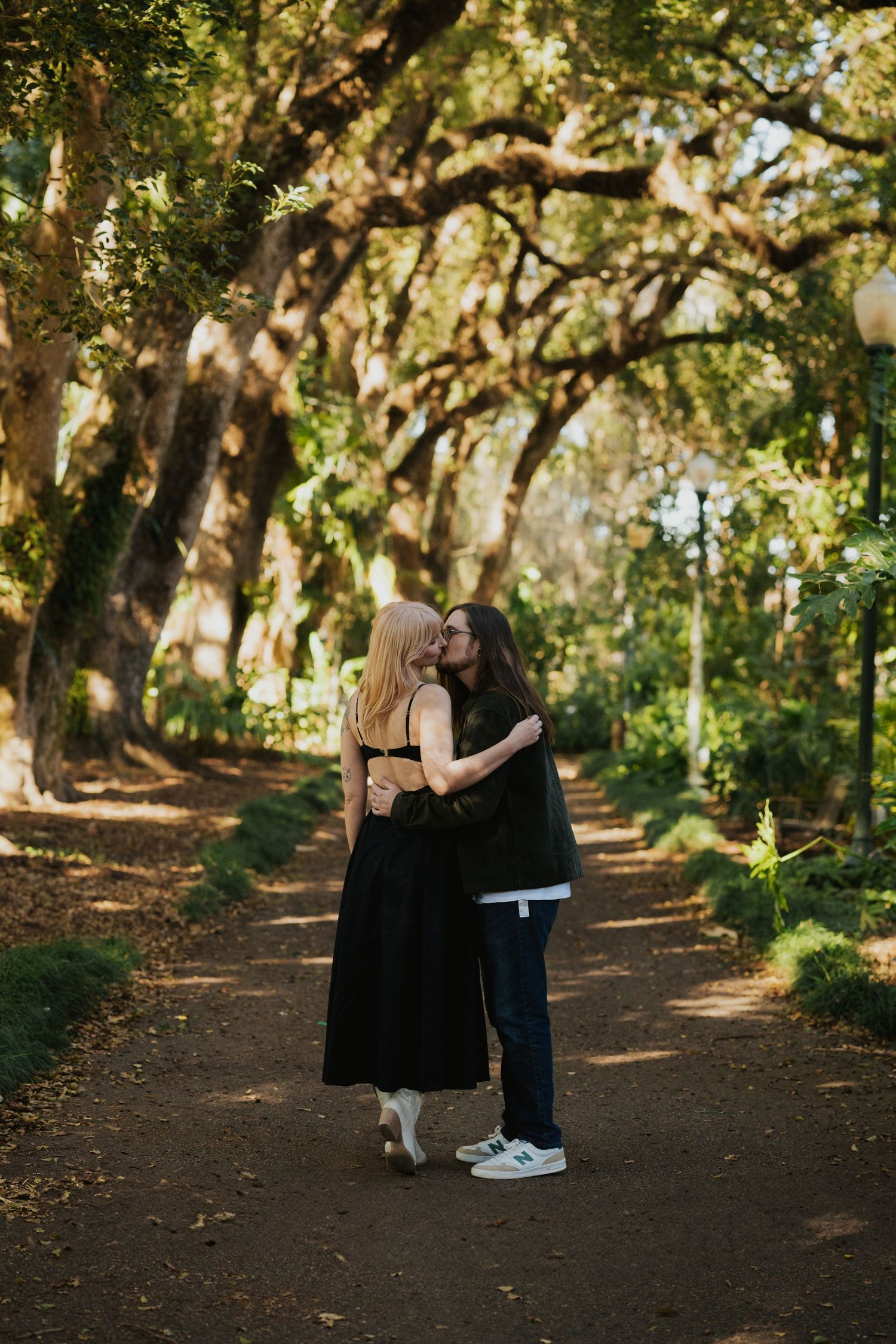 Two people share an intimate moment while standing on a wooded trail.