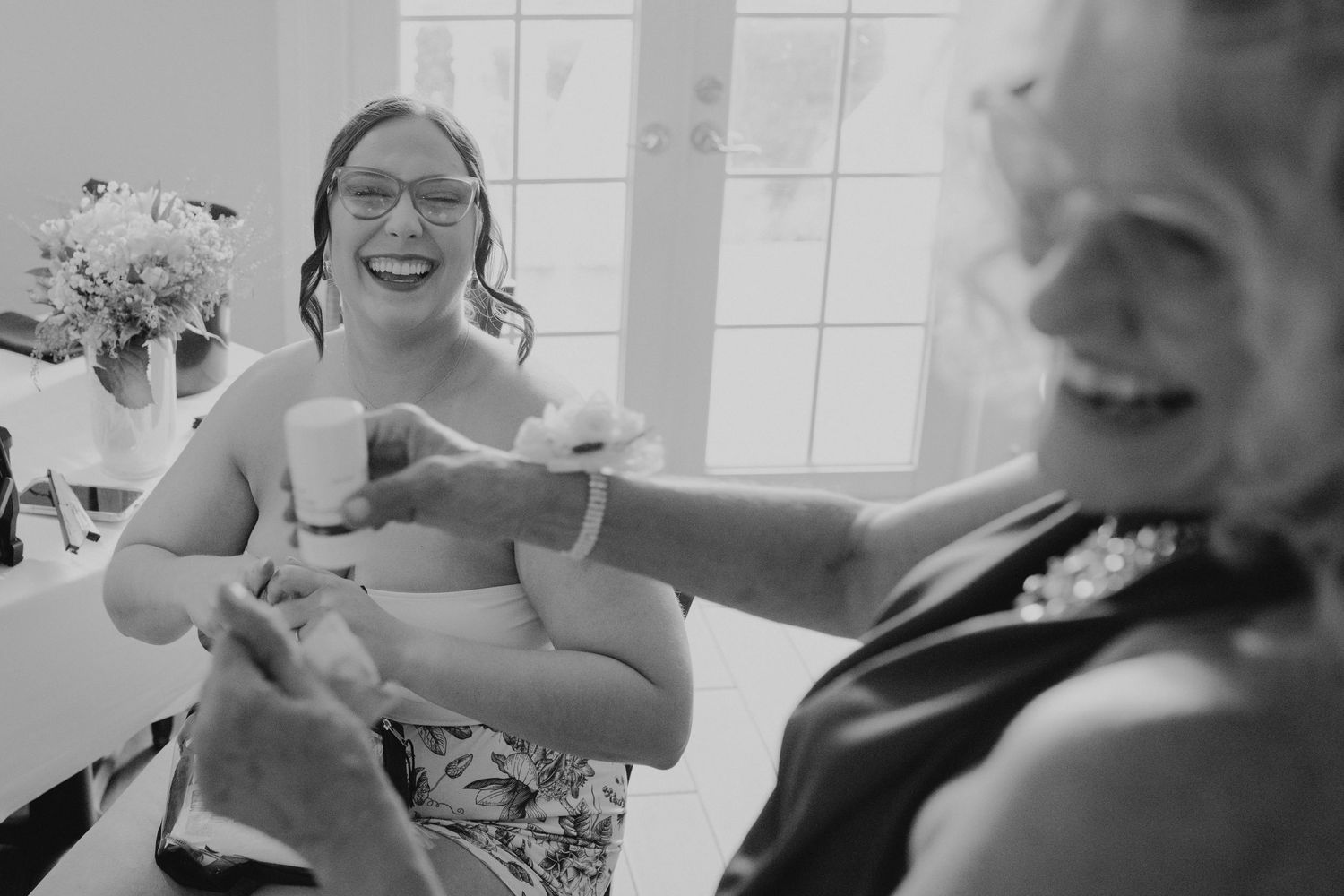 A joyful black and white candid moment between two people laughing and interacting at a social gathering.