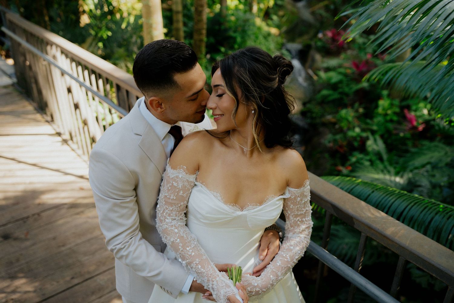 A couple shares intimate moments on a wooden bridge surrounded by lush tropical greenery.
