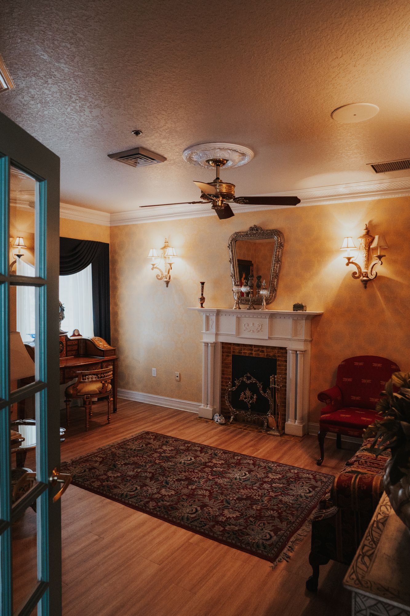 Elegant sitting room with fireplace, ornate mirror, and vintage furniture on hardwood floors.