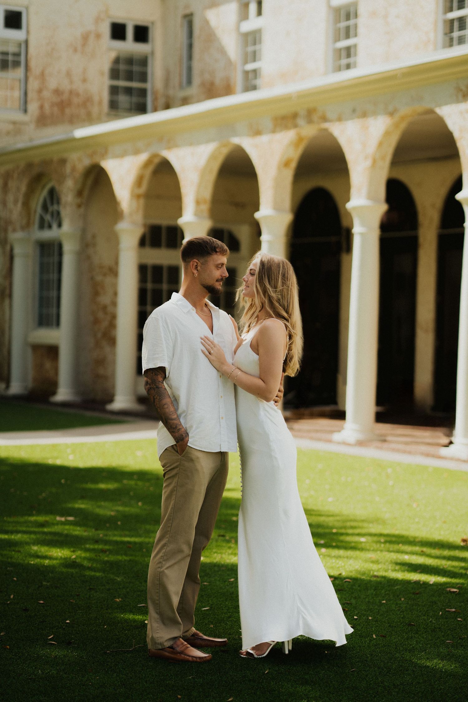 A romantic couple poses in front of a beautiful colonnade with arches on a sunny day.