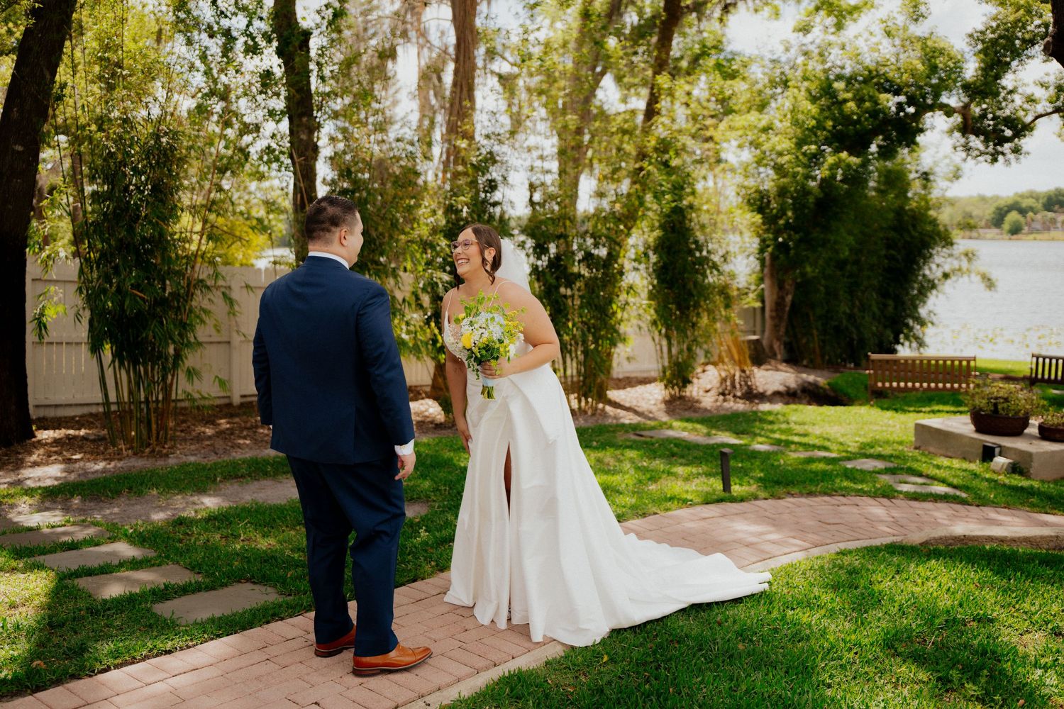 Two people share a special moment in a lush garden setting with a stone pathway and green lawn on a sunny day at enzos on the lake.