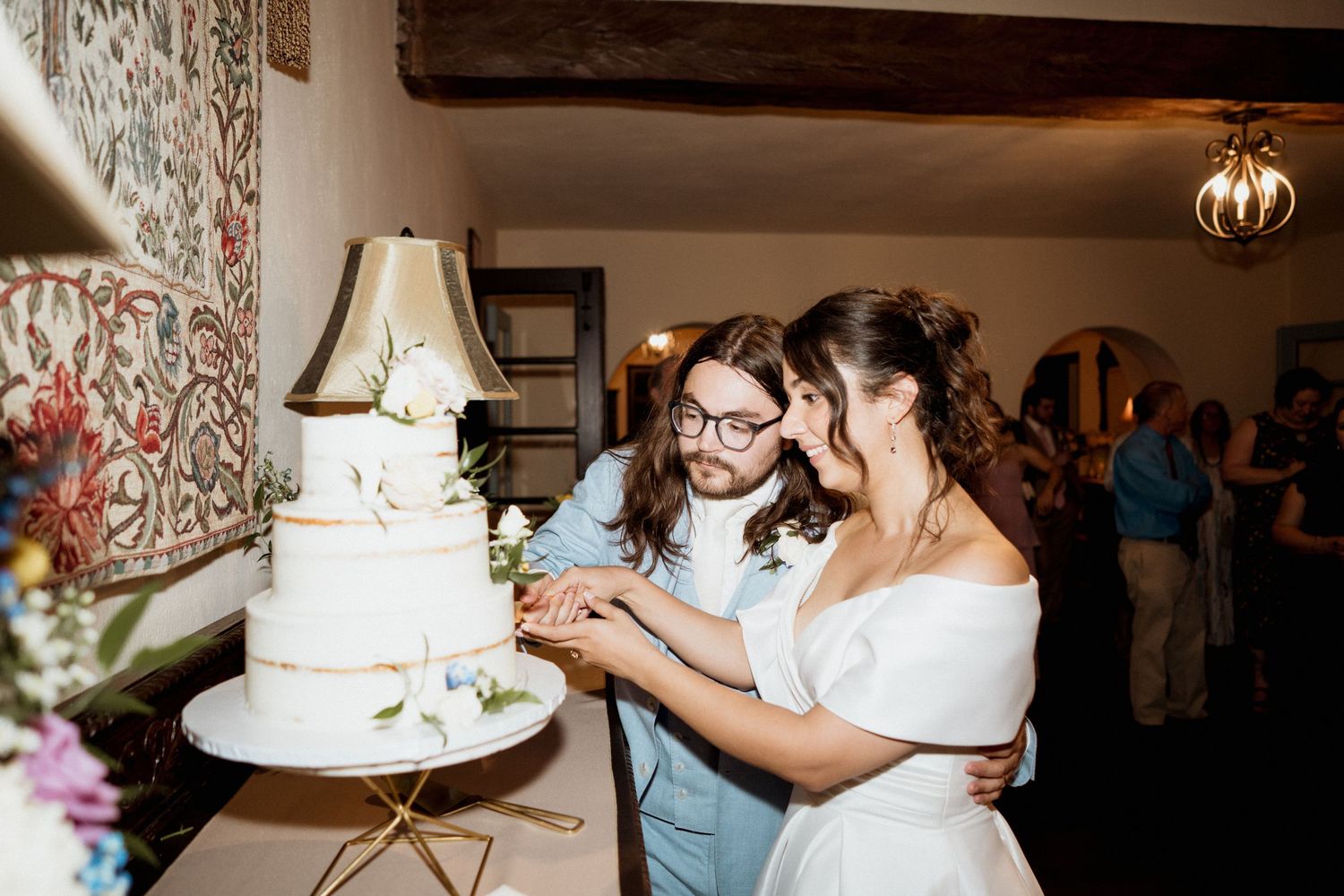 A wedding cake cutting moment at an indoor reception with an elegant three-tiered white cake.