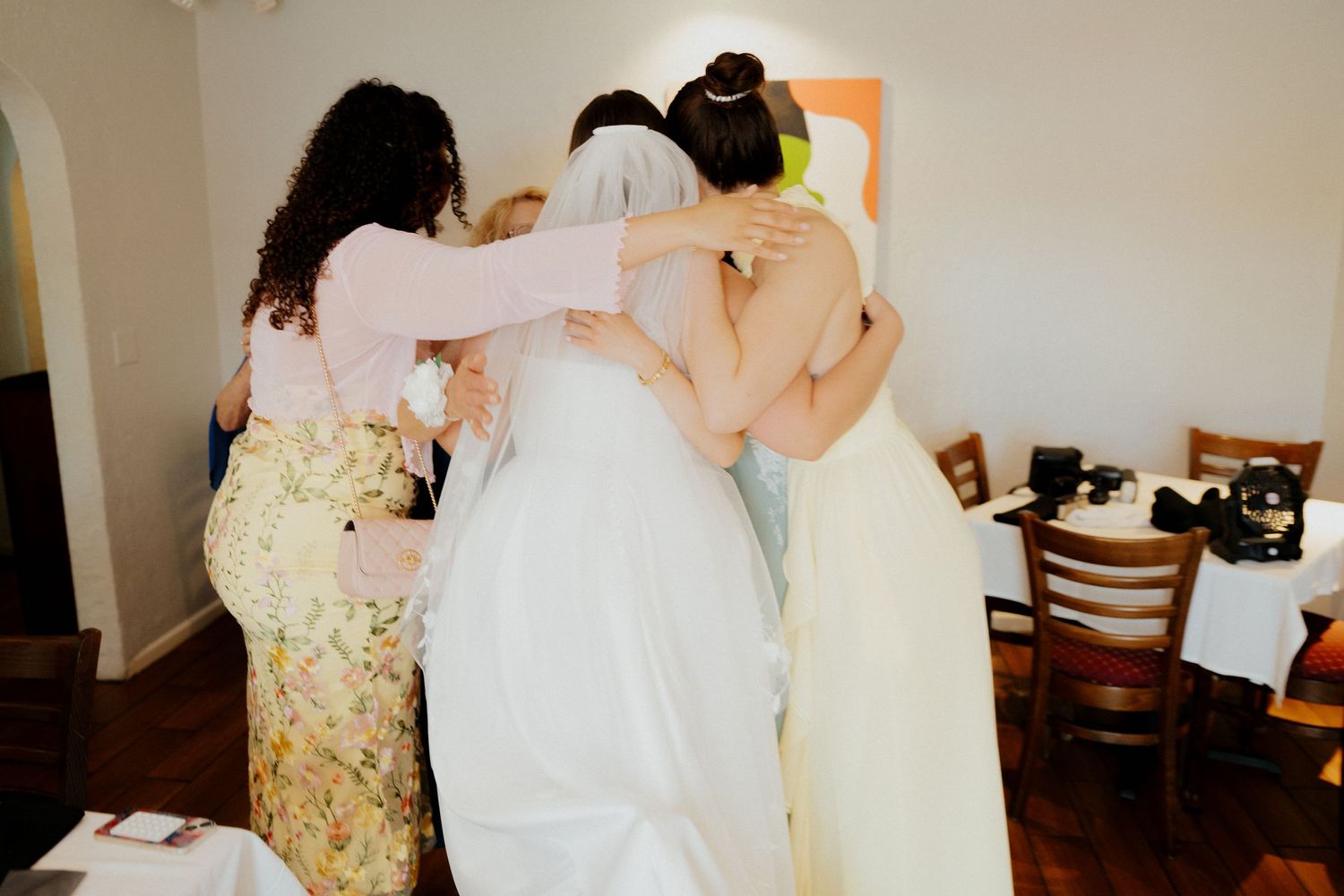 Three celebrants in formal dresses share an intimate embrace during a special occasion.
