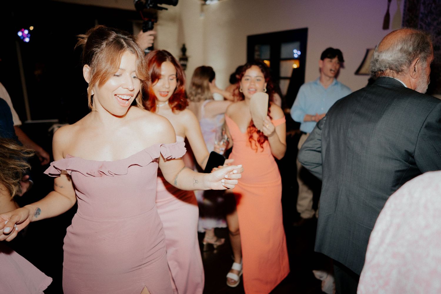 People dancing and socializing at what appears to be a wedding reception or party in a dimly lit venue.