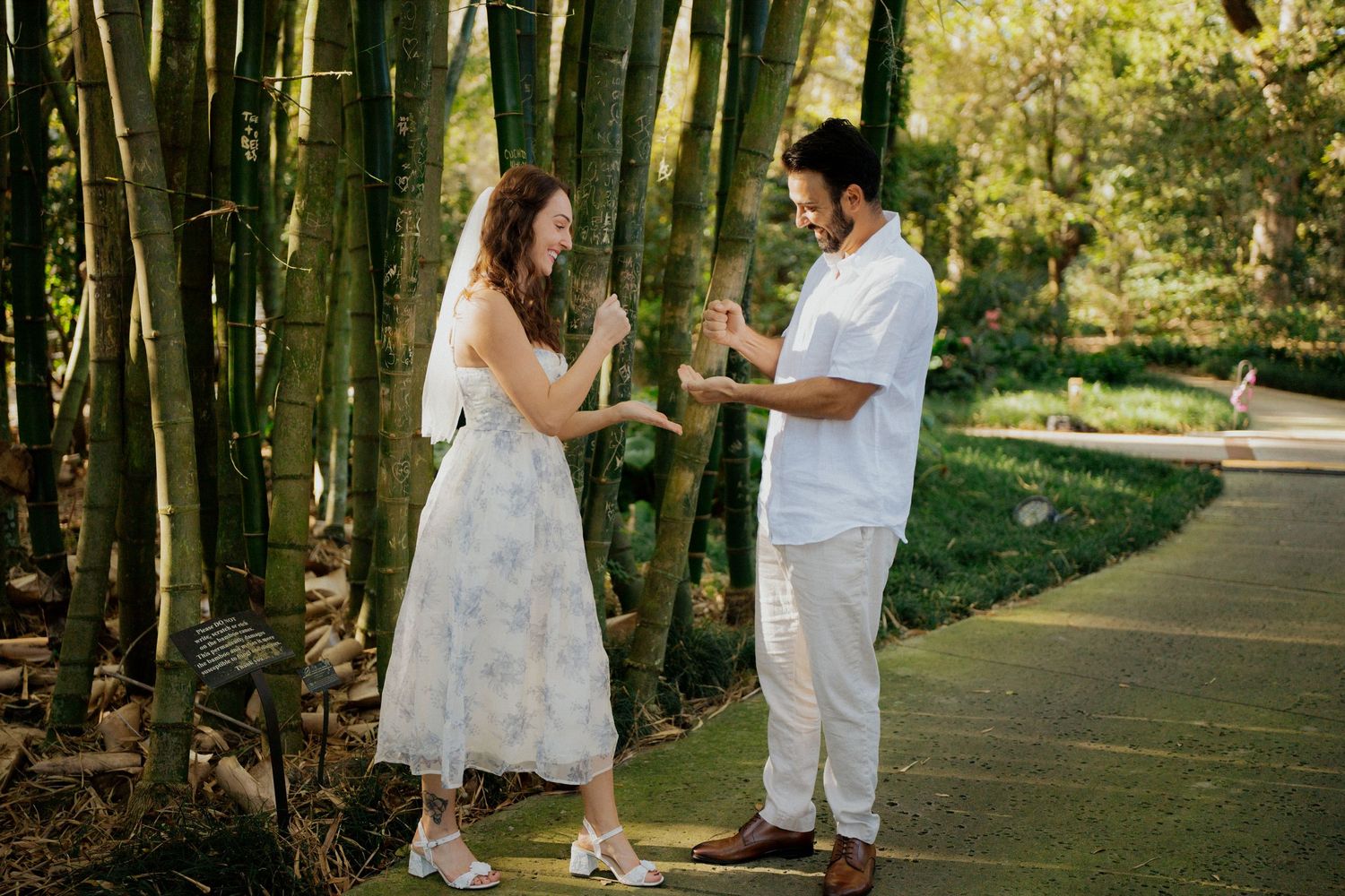 A couple in white attire shares a romantic moment on a tree-lined path during a wedding photo session  at Harry P Leu Gardens