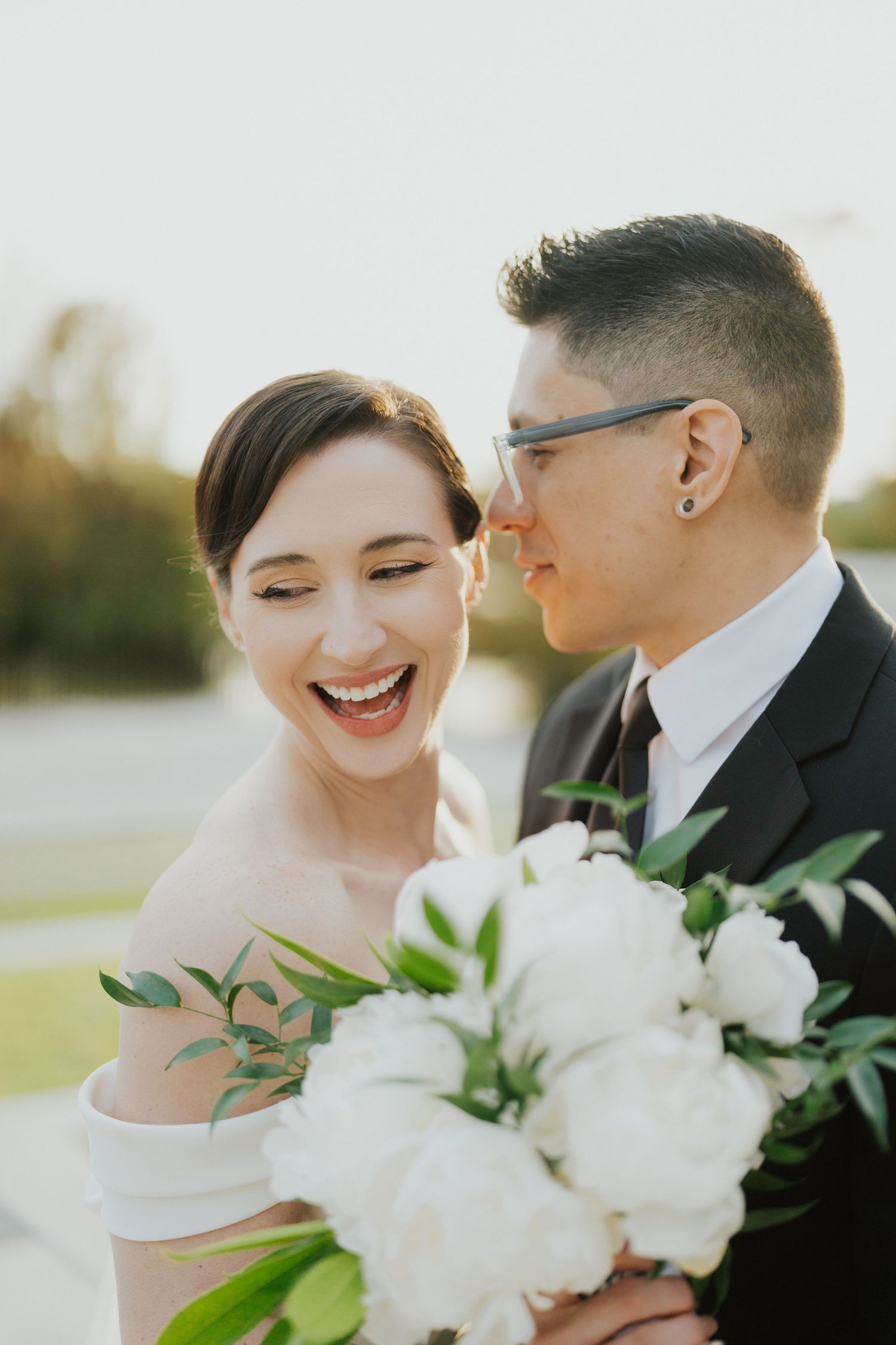 A couple in wedding attire share intimate moments while holding a white floral bouquet during their outdoor photoshoot.
