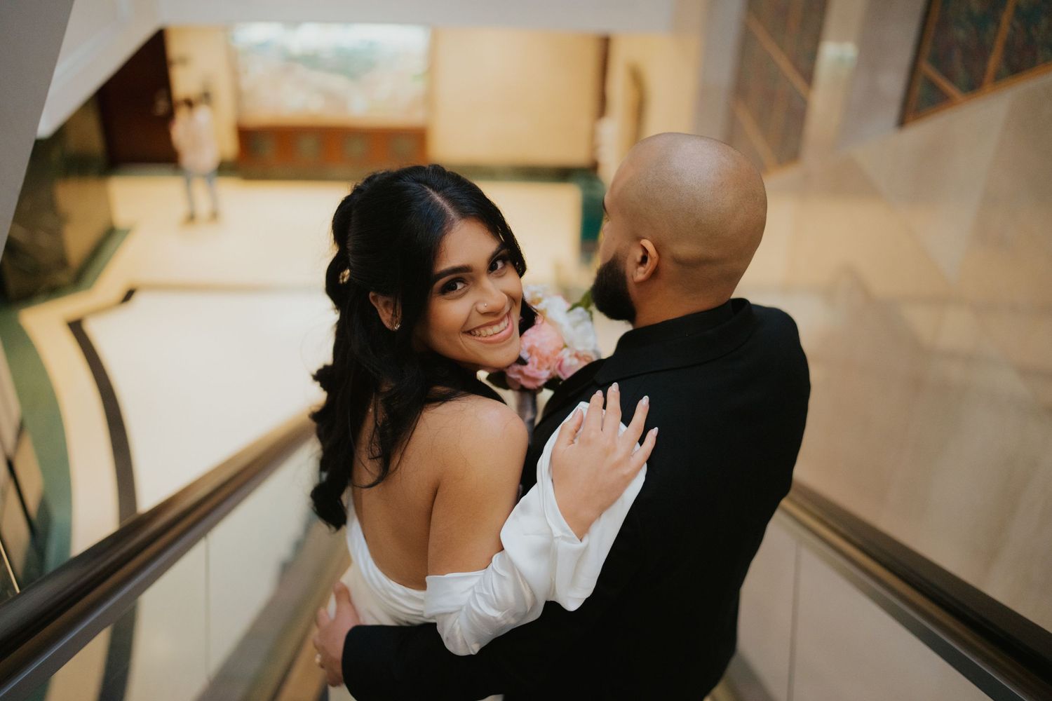 A romantic couple sharing an intimate moment on an escalator in formal attire.
