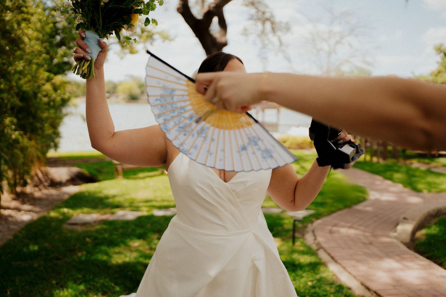 Dancing figure in a white dress holding a decorative fan outdoors in a sunlit garden setting.