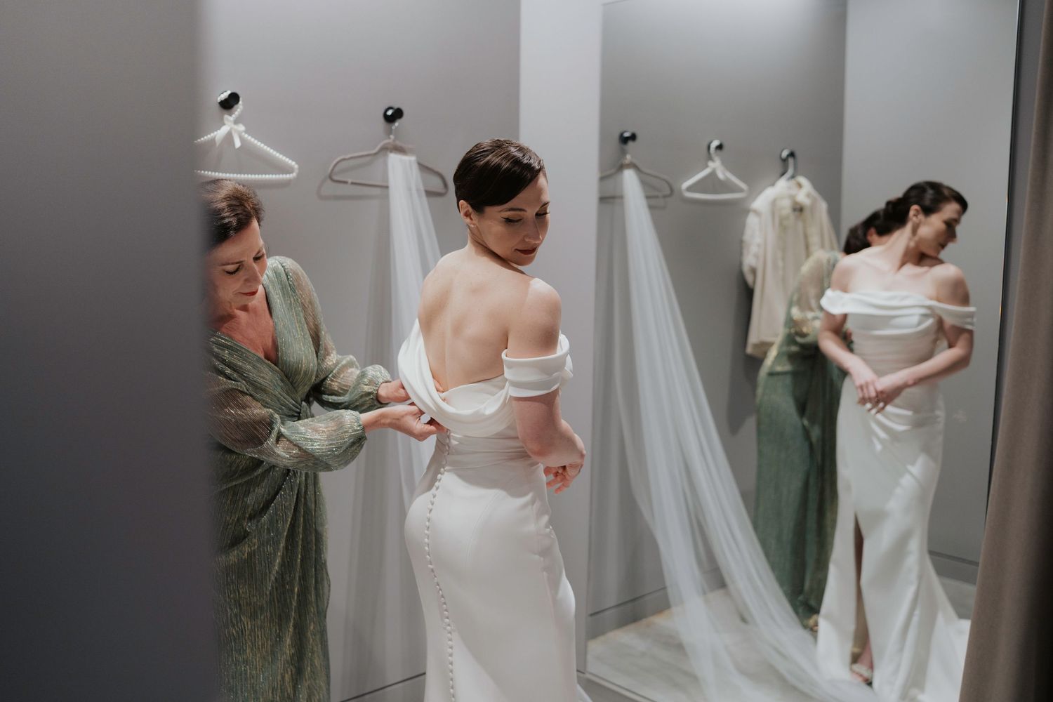 A bride in a white wedding dress gets help with final adjustments during a getting ready moment.
