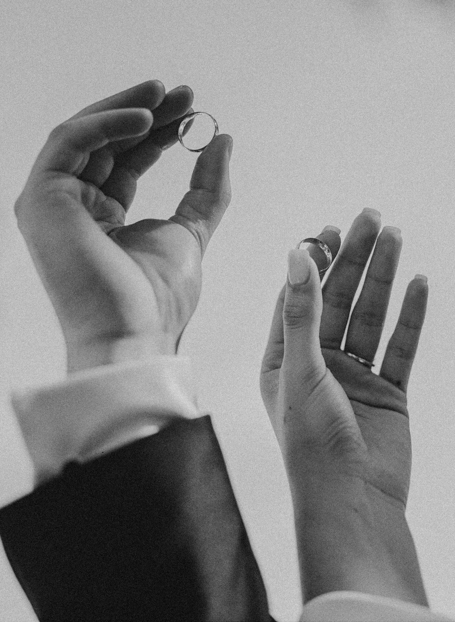 Black and white close-up of two hands holding wedding rings during a wedding ceremony.