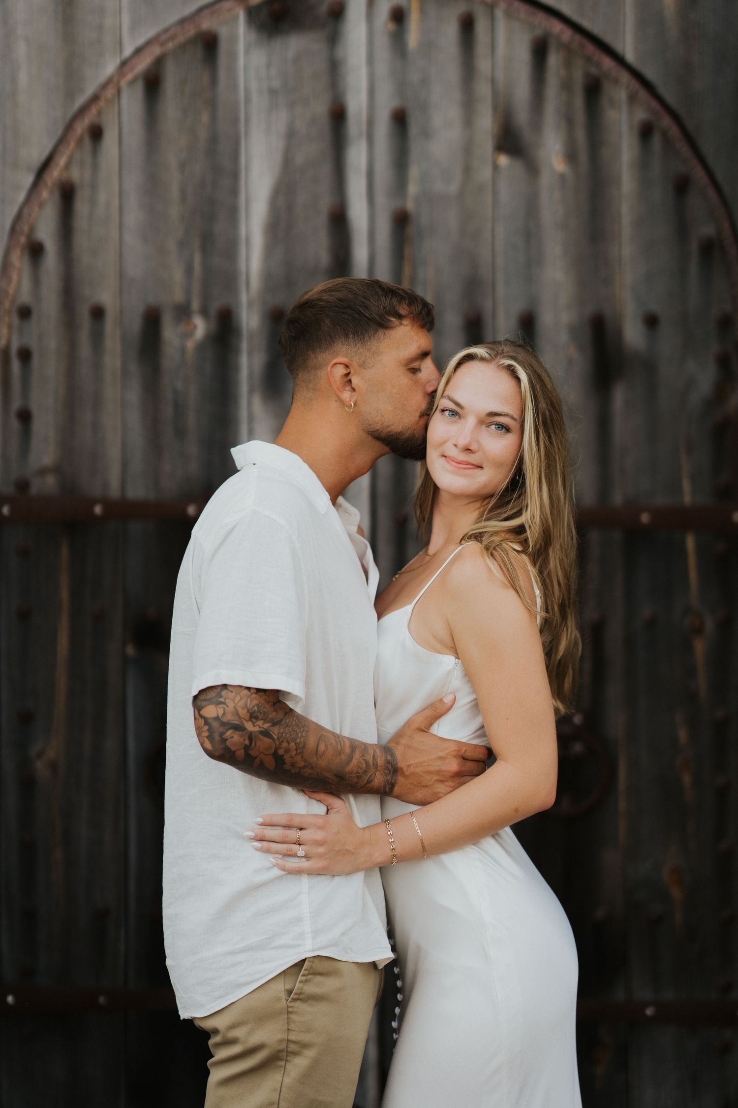 A romantic couple embraces against a rustic metal wall background.