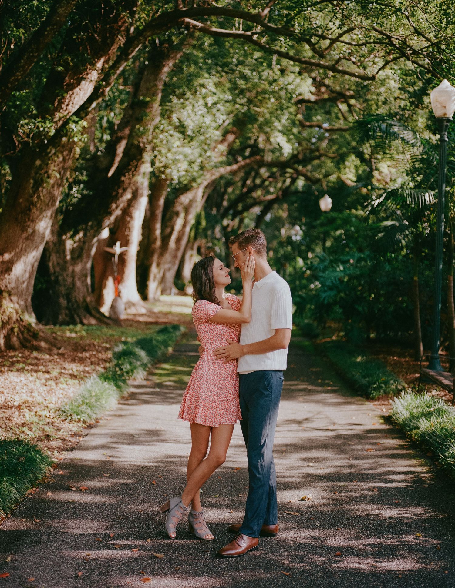 A couple shares a romantic moment on a tree-lined path during their engagement photoshoot.