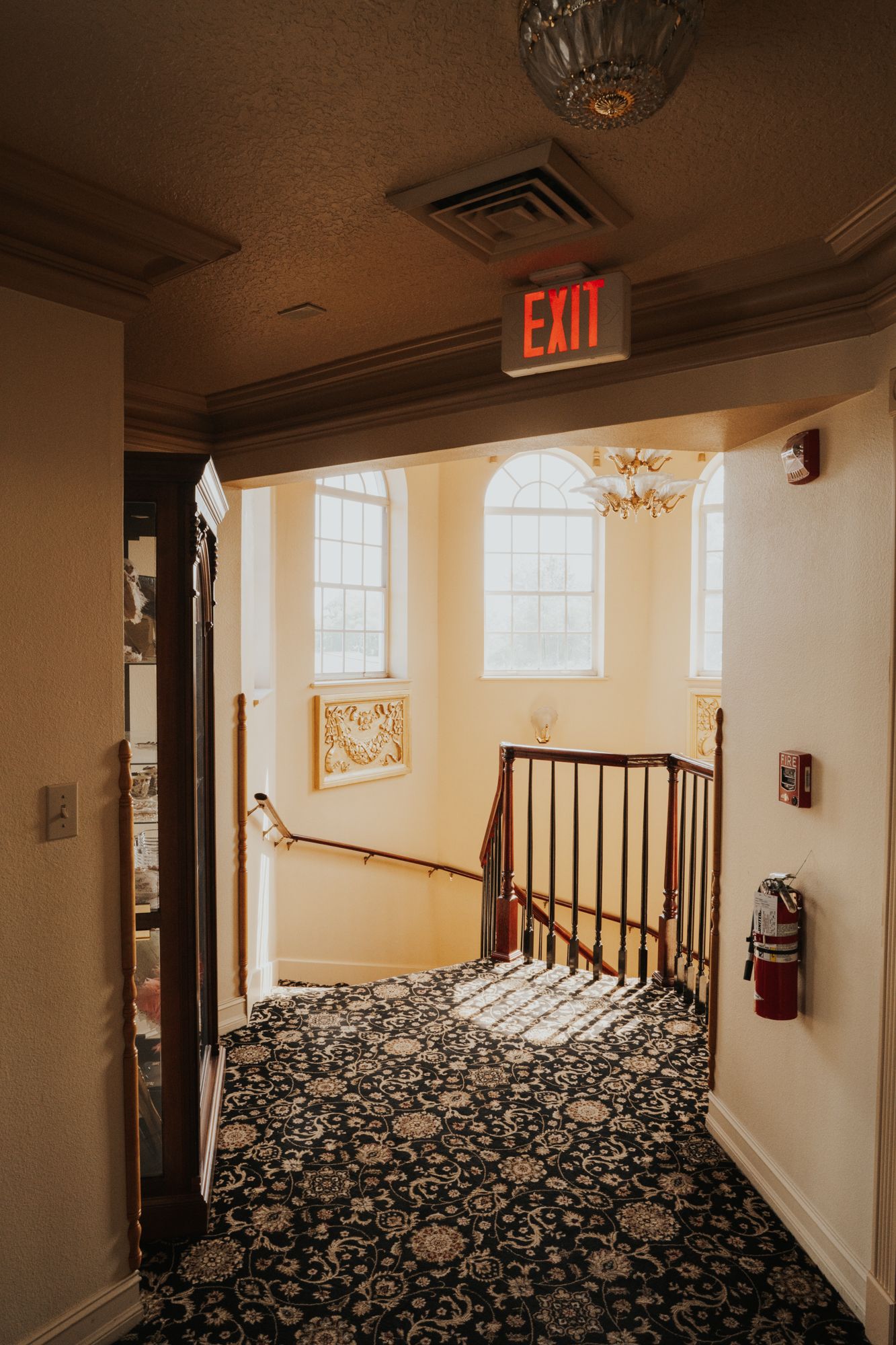 Interior hallway with floral carpet, arched windows, and illuminated exit sign.