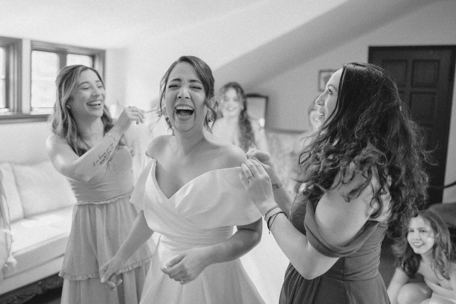Black and white candid photo captures joyful laughter during wedding preparation moments.