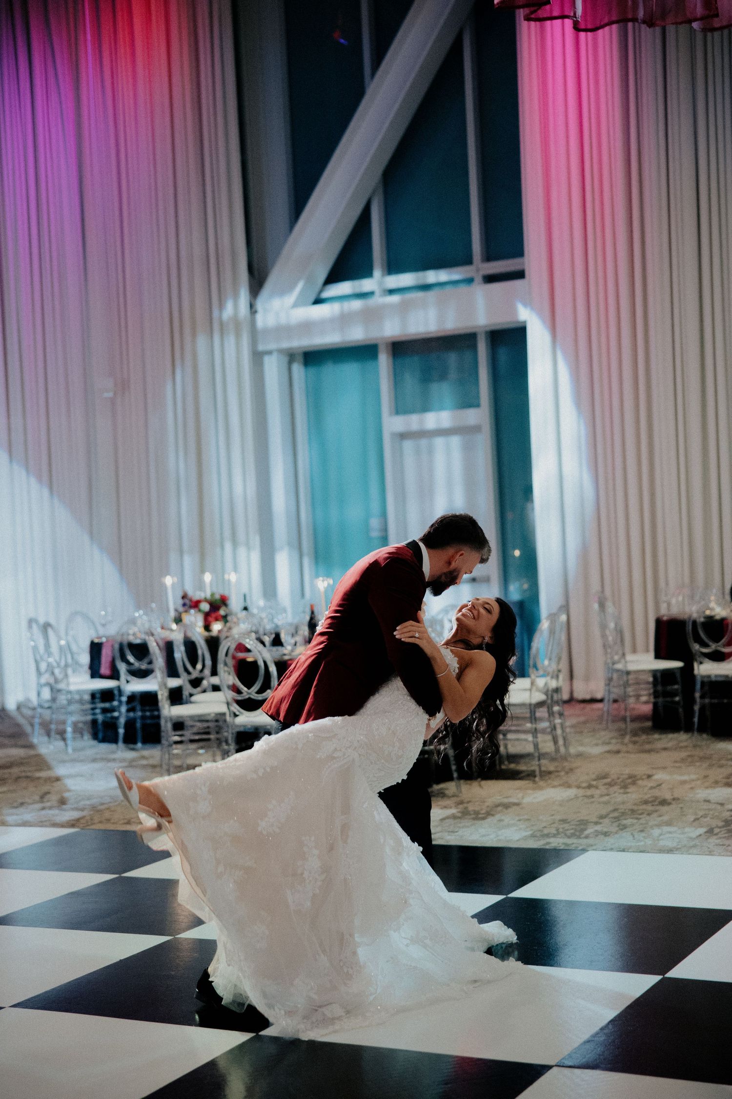 Bride and groom share romantic dip on black and white checkered dance floor at wedding.