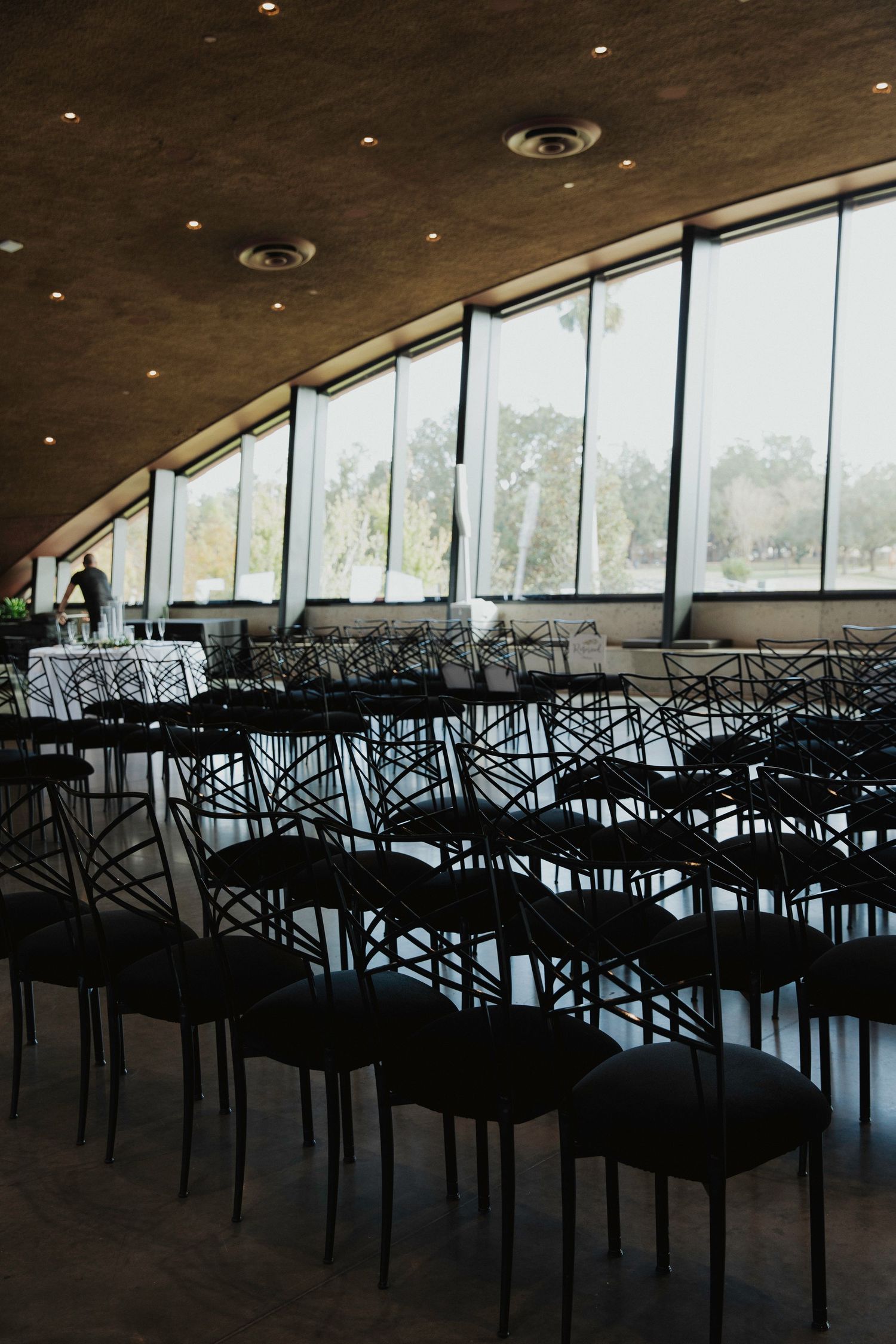 Empty banquet chairs arranged in rows inside a modern venue with large curved windows and natural lighting.