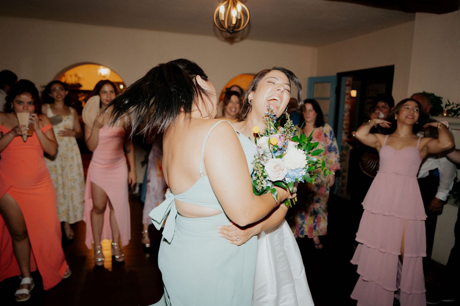 Wedding celebration with dancing and laughter as a bouquet is shared between guests in formal attire.