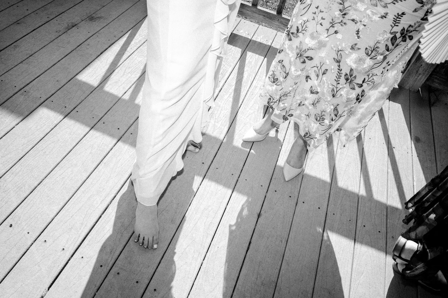 Black and white photo of bride in white gown standing on wooden deck with shadow.