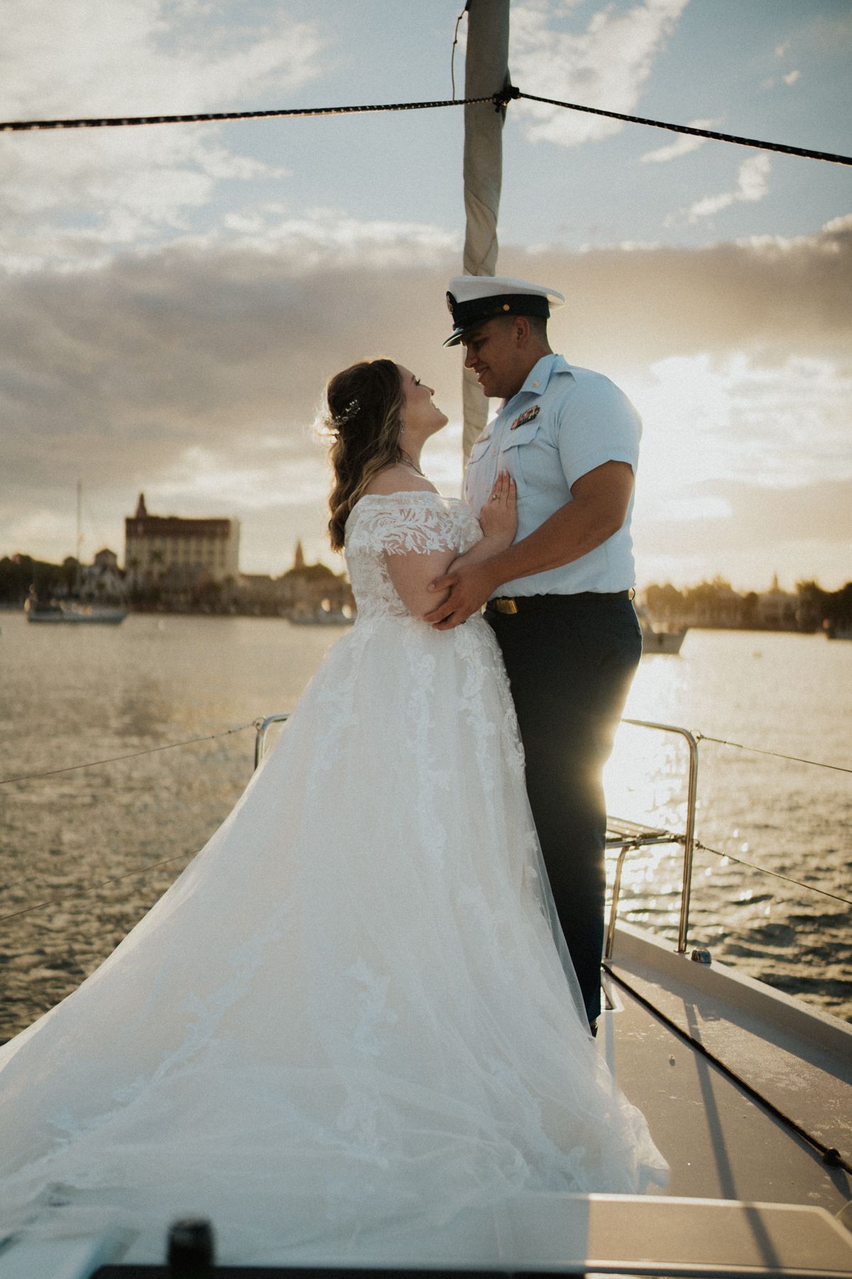A couple shares an intimate moment on a boat deck during sunset by the water.