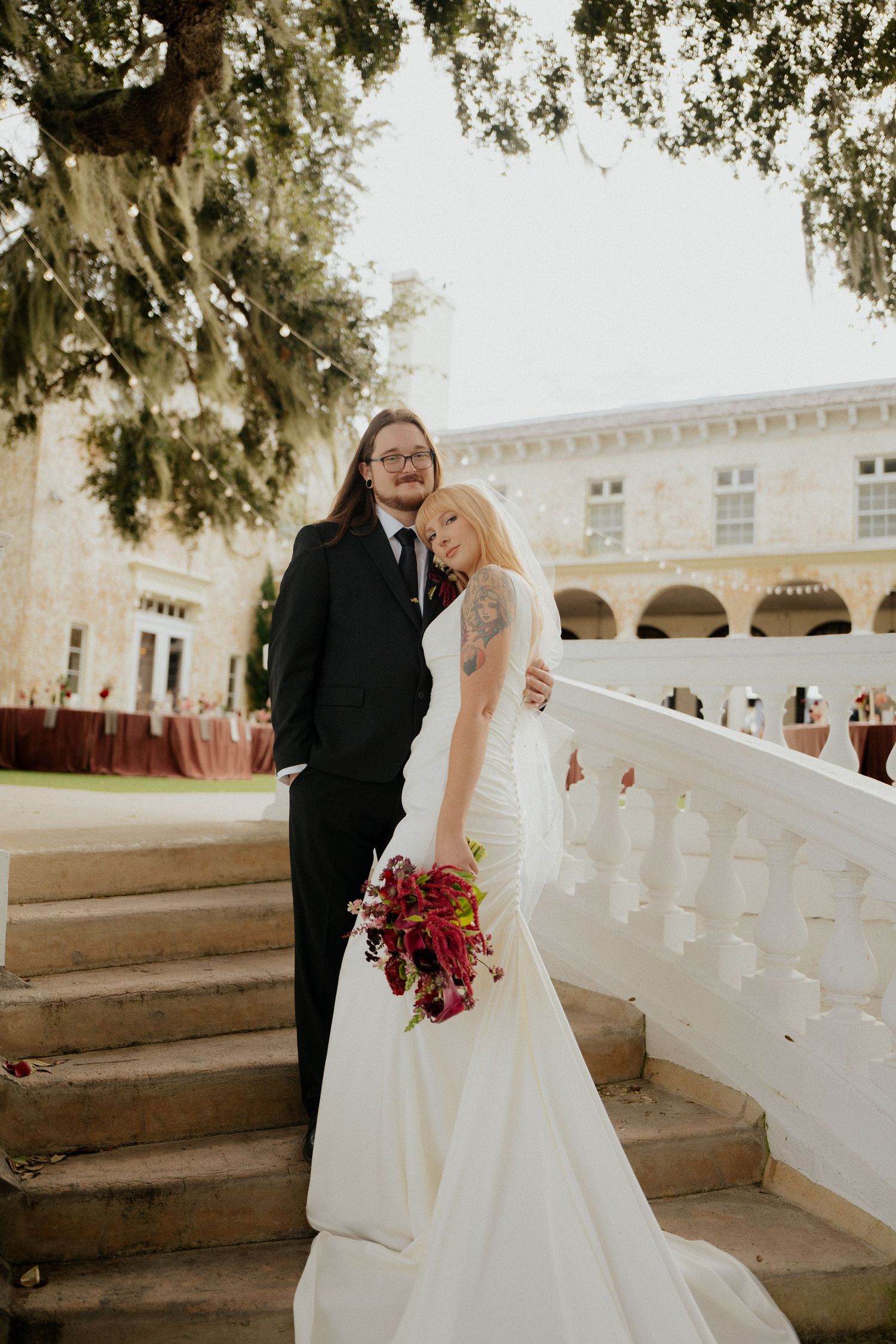 Bride and groom pose on stone steps outside a grand venue with Spanish-style architecture.