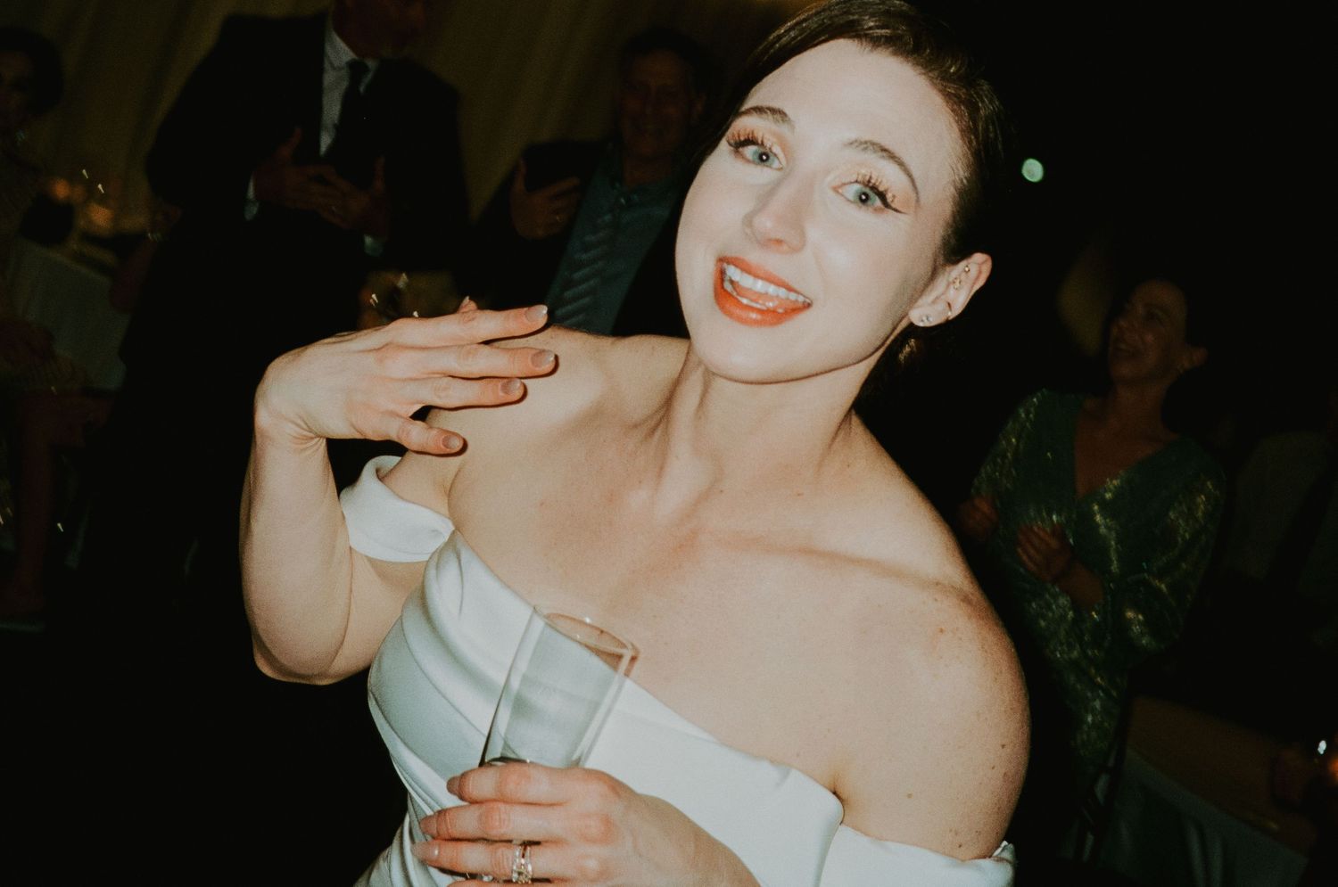 Elegant woman in white off-shoulder dress dancing and smiling at a wedding reception.