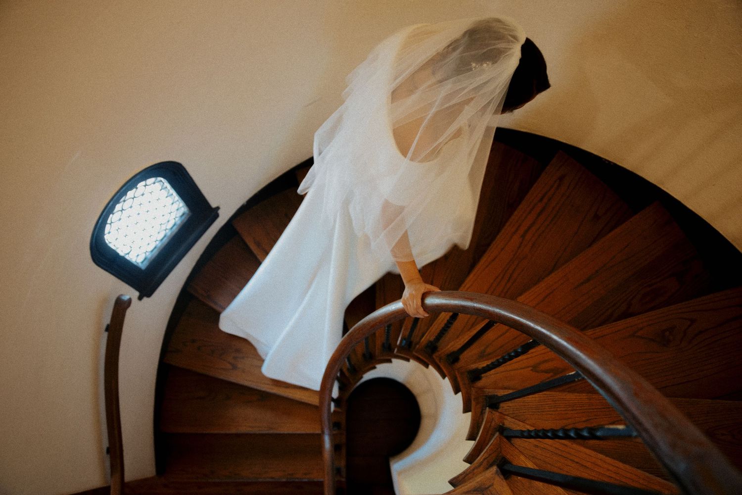 A white wedding dress trails down dark wooden stairs in warm lighting.