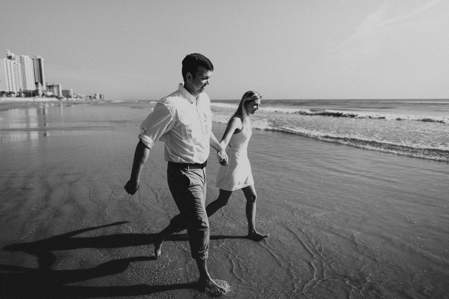 A couple walking playfully along the beach shore in black and white photography.