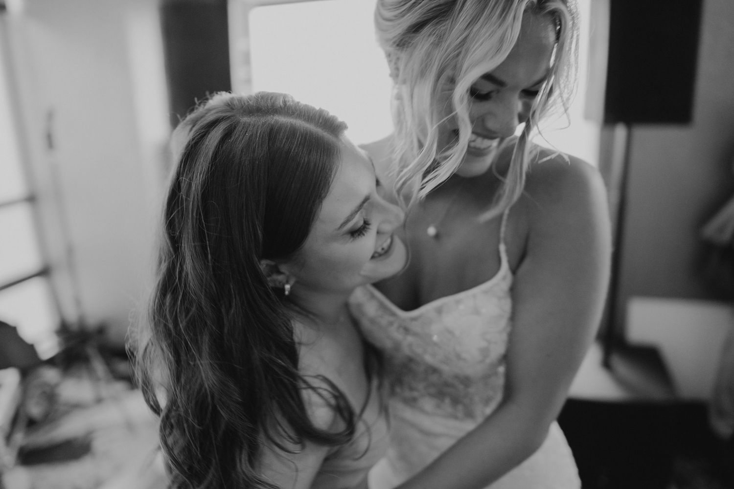Black and white photo of bridesmaid helping bride with her lace wedding dress before the ceremony.