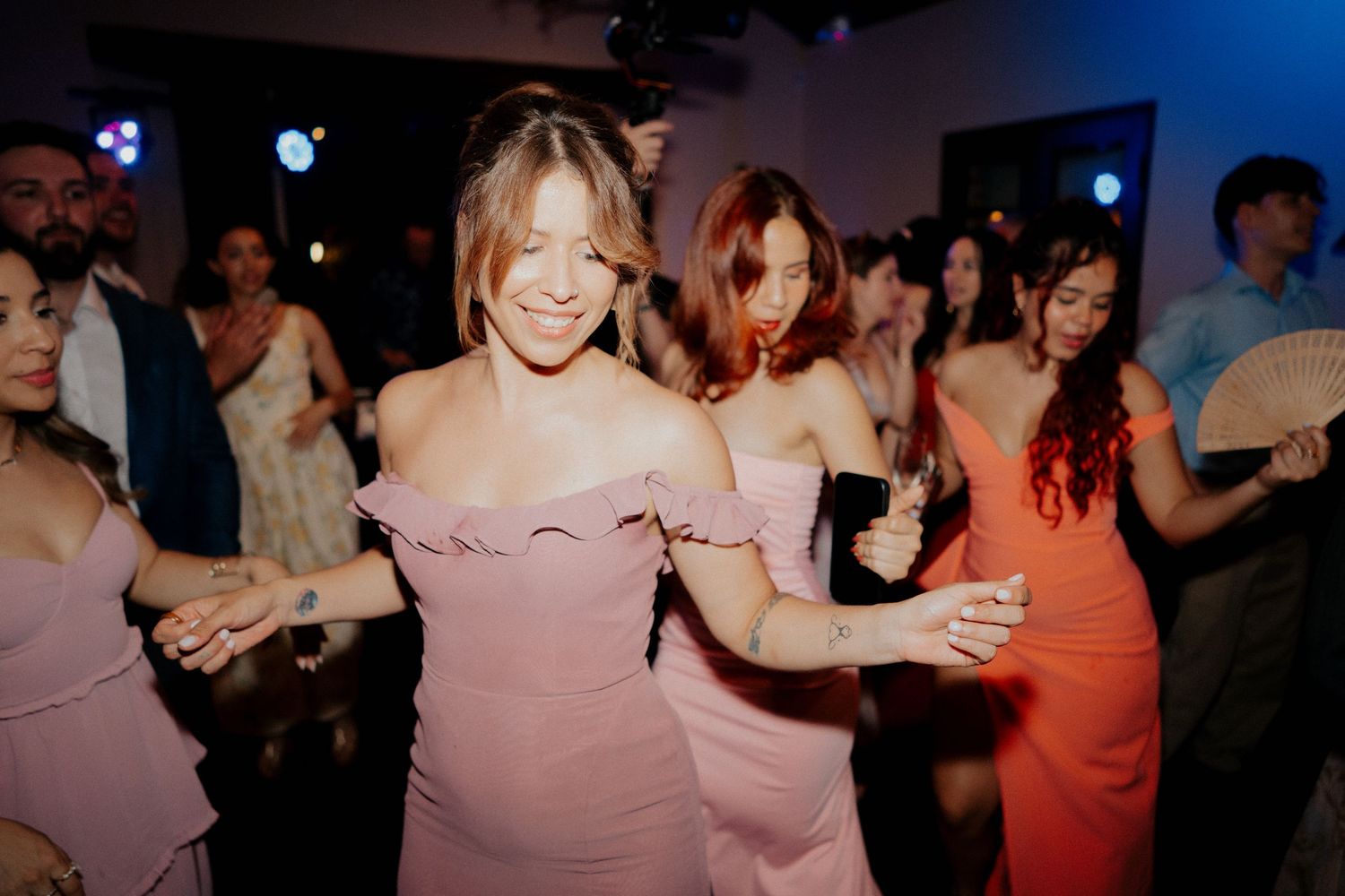 Wedding reception dance party with guests in colorful attire under dim lighting.