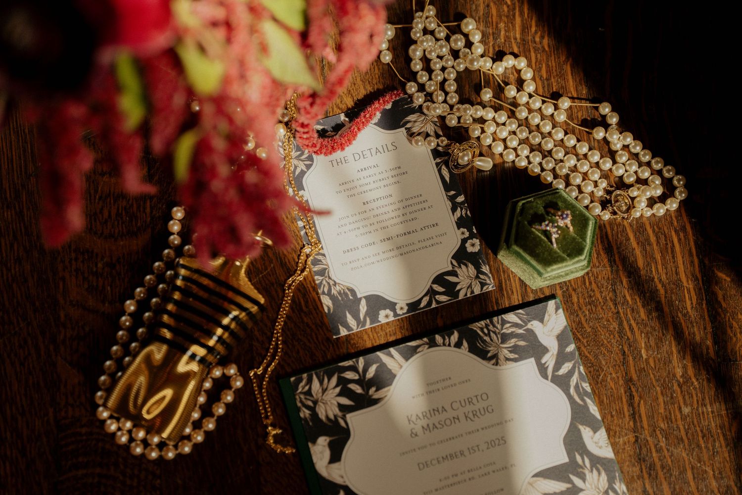 Wedding invitation suite with gold jewelry and floral details arranged on rustic wooden surface.