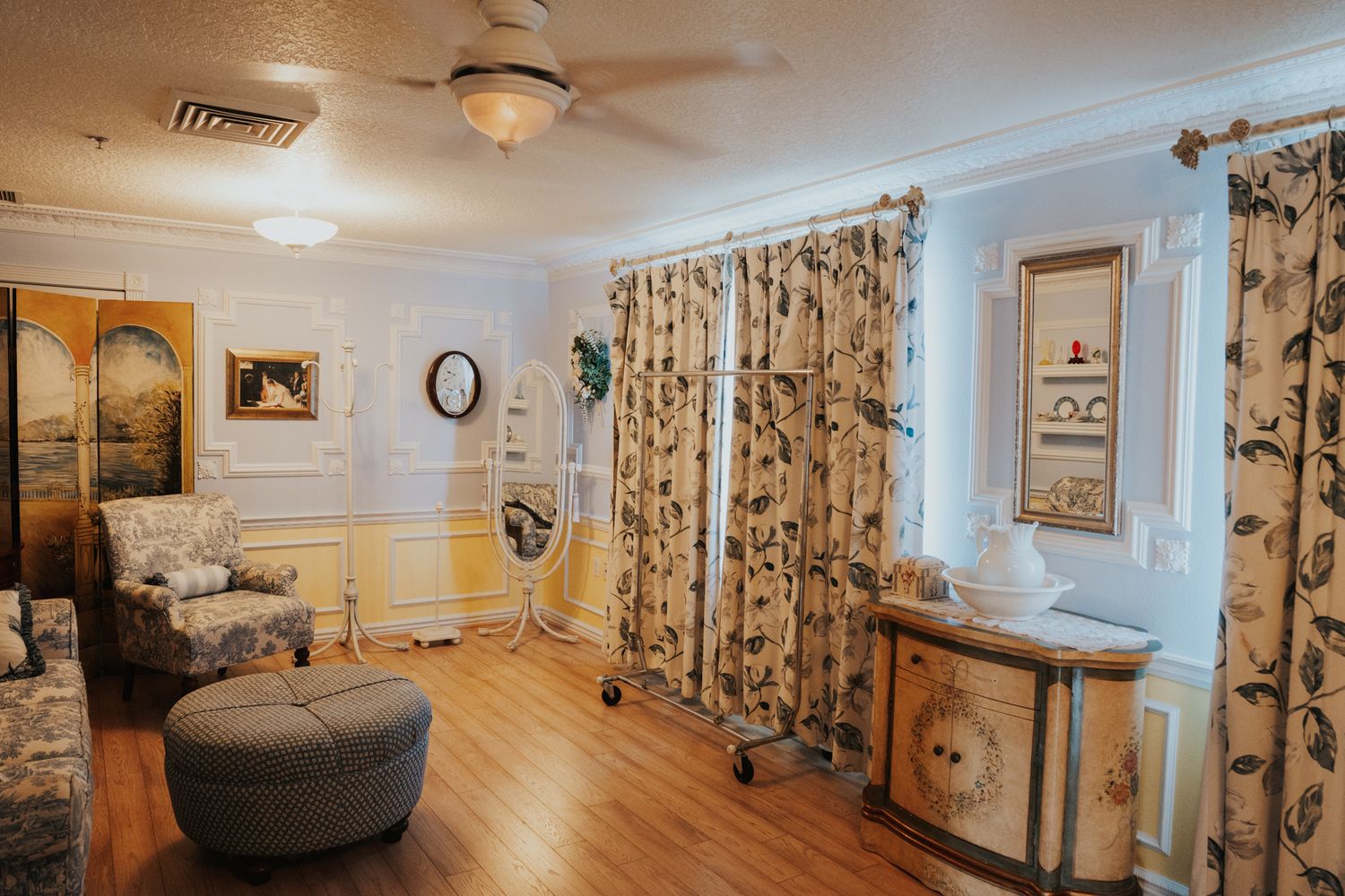 Cozy sitting room with floral curtains, vintage furniture, and hardwood flooring.