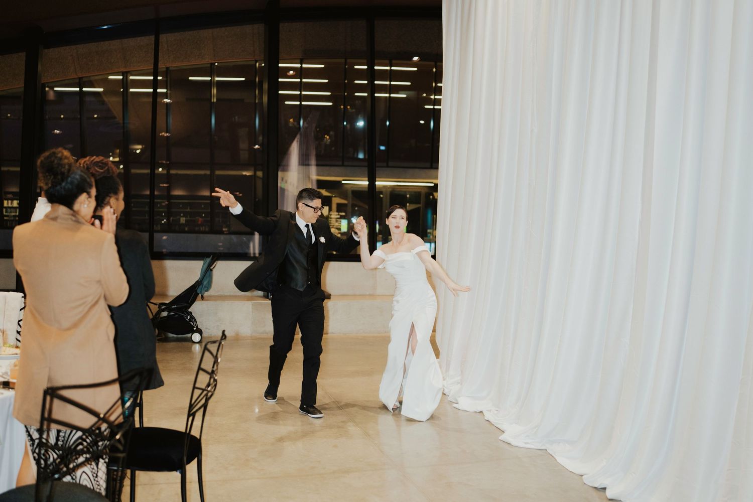 Wedding ceremony setup with white curtains and guests gathering in a modern venue.