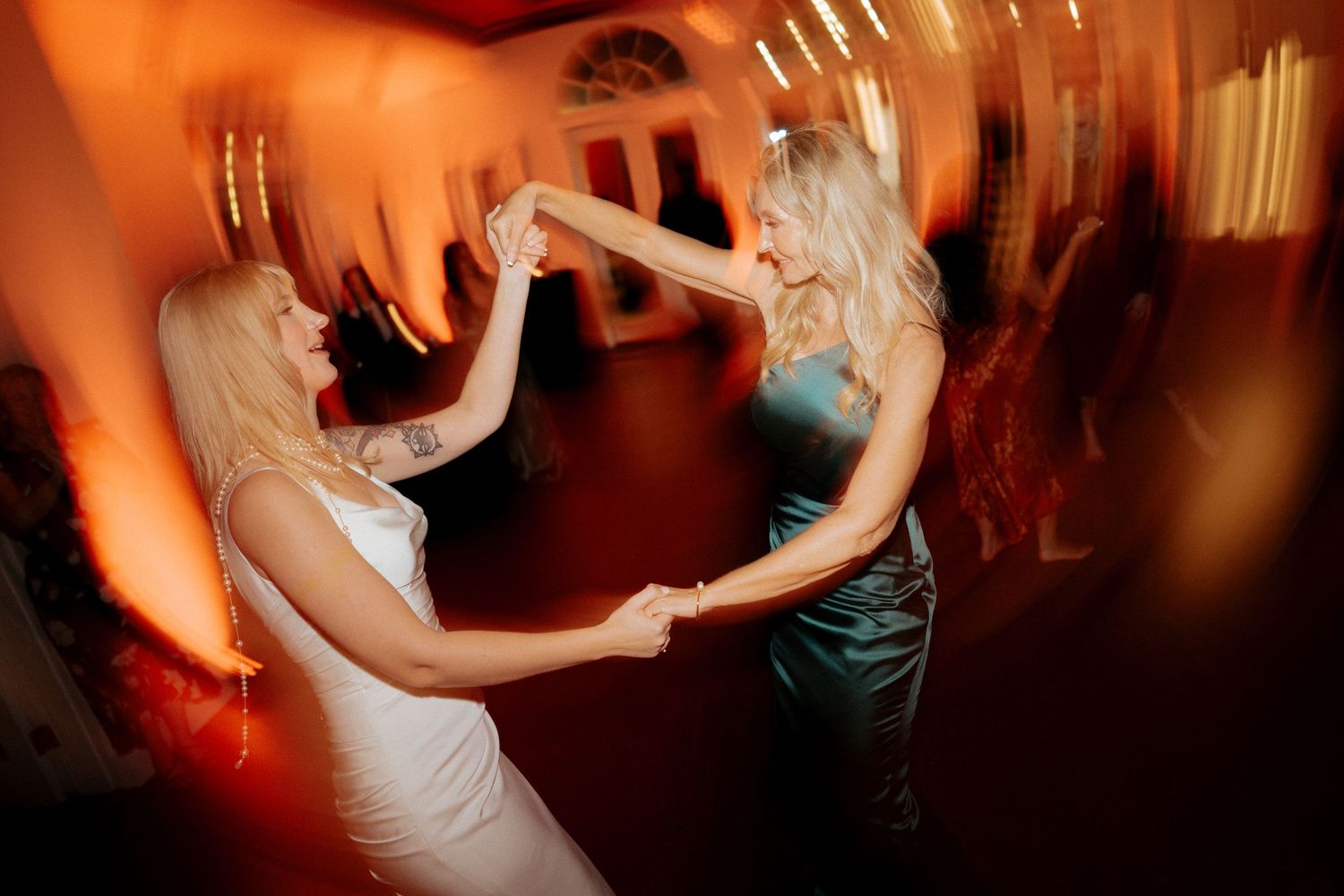 Wedding guests dancing and celebrating on a dimly lit dance floor with warm orange lighting.