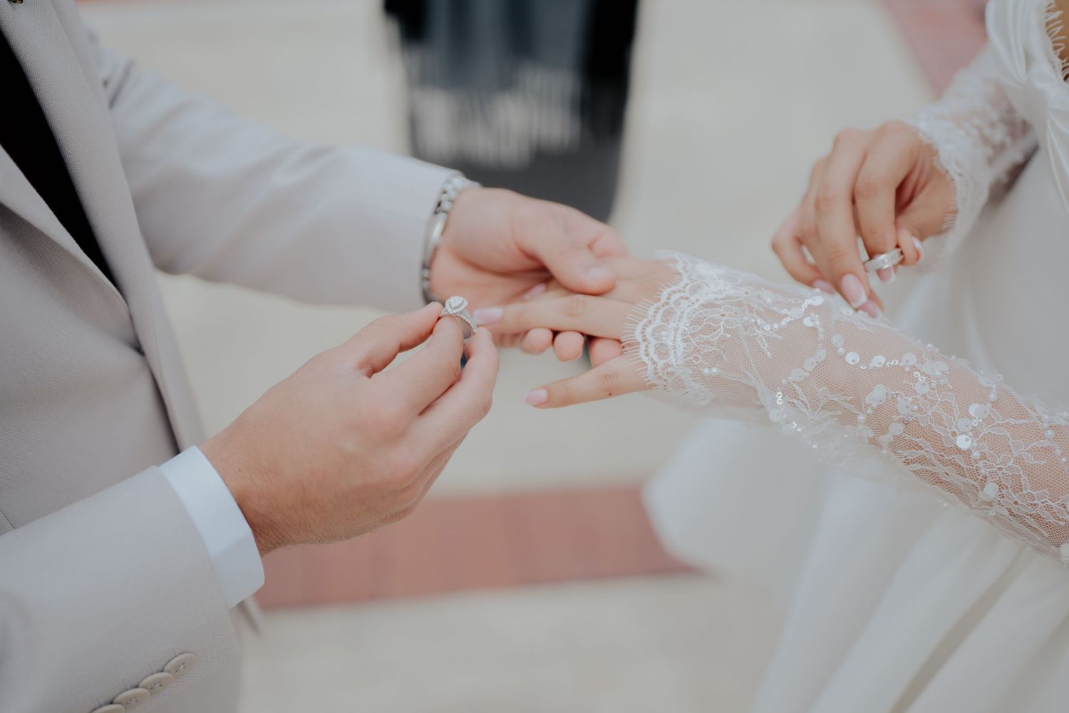 Close-up shot of hands exchanging rings with delicate lace details during a wedding ceremony.