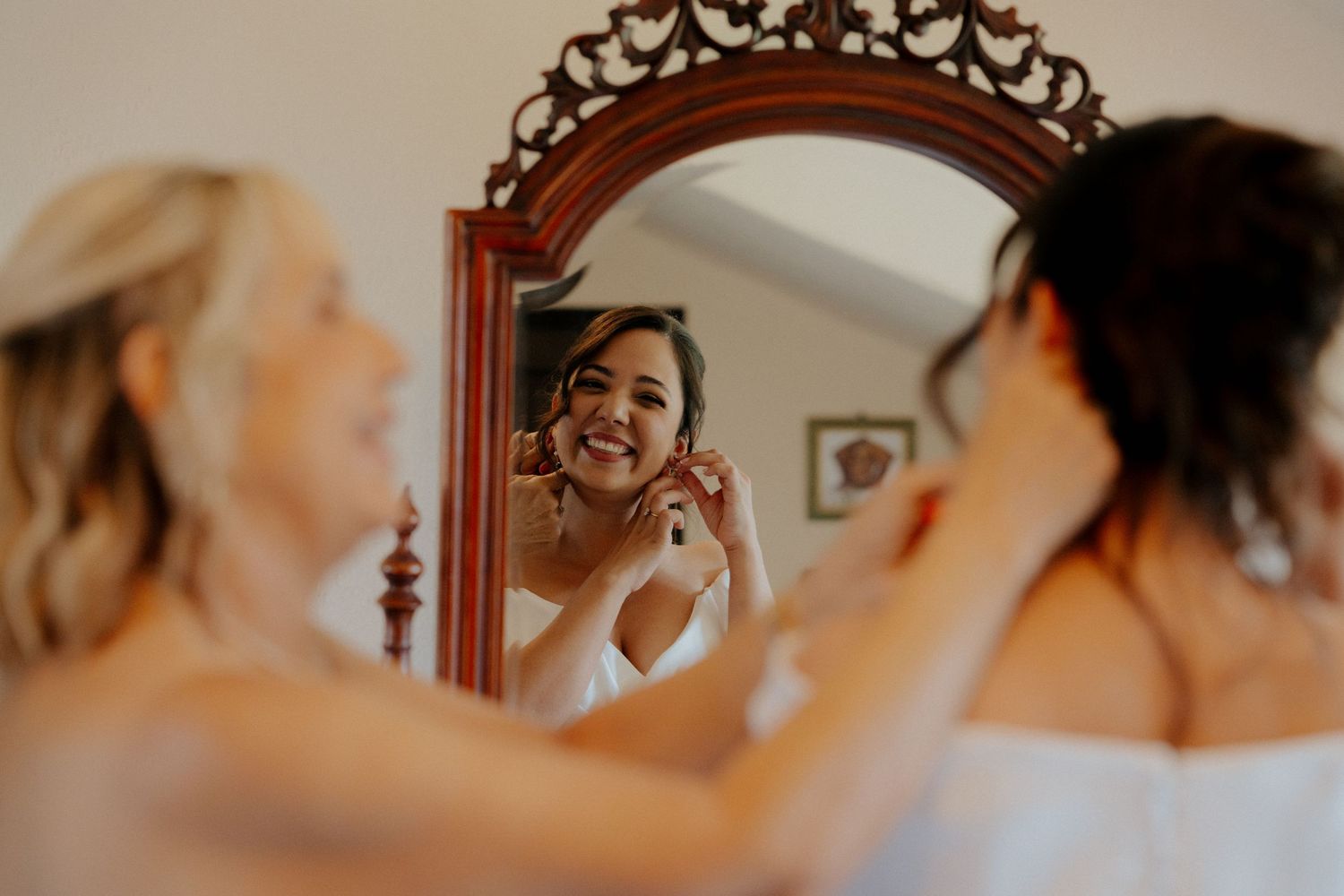 Bride getting ready in front of ornate mirror with warm lighting and vintage decor.