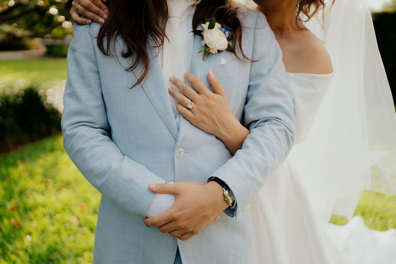 Wedding couple in white and light blue attire embracing in an outdoor garden setting.