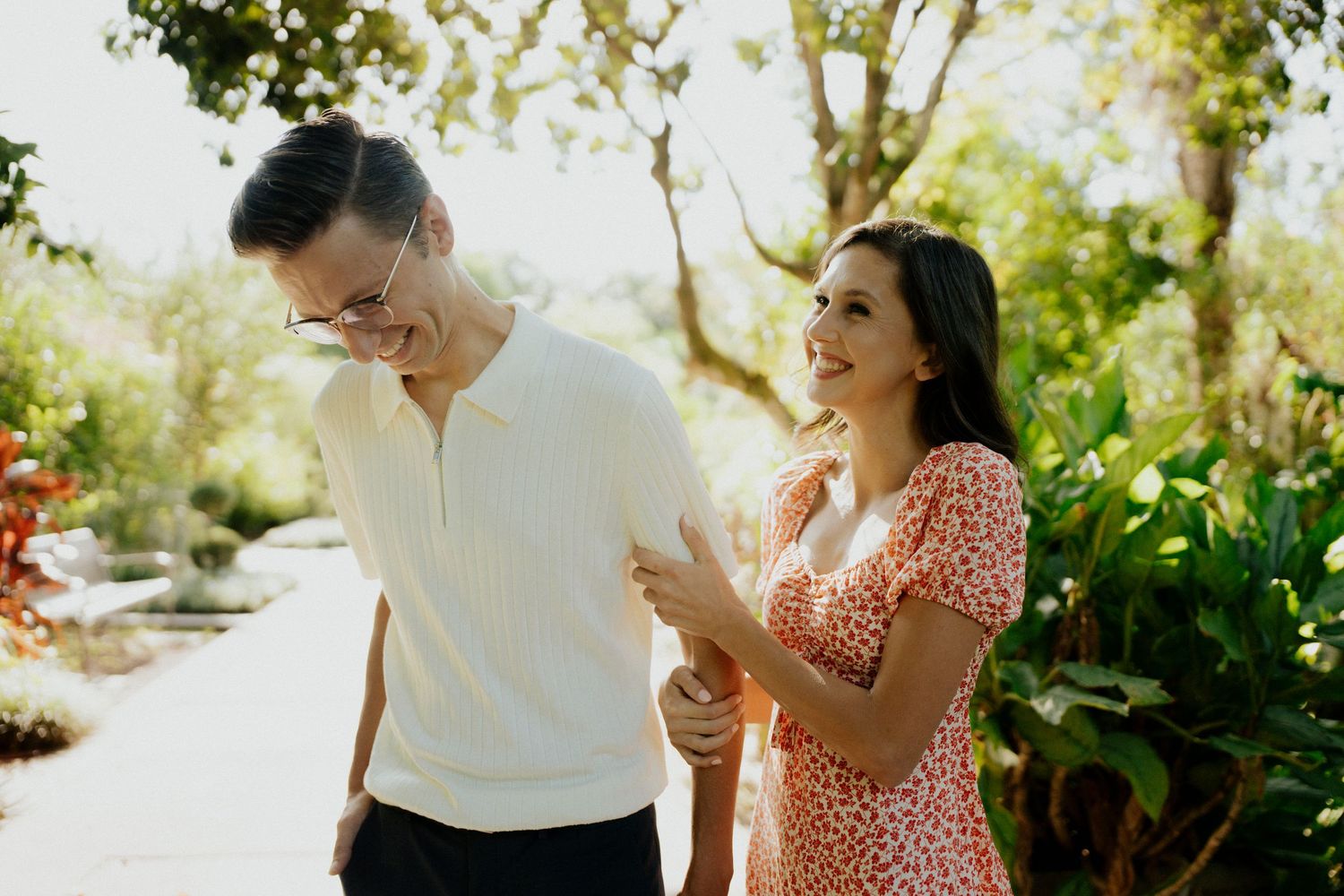 A couple enjoys a romantic outdoor picnic with wine glasses in a lush garden setting during a sunny afternoon.