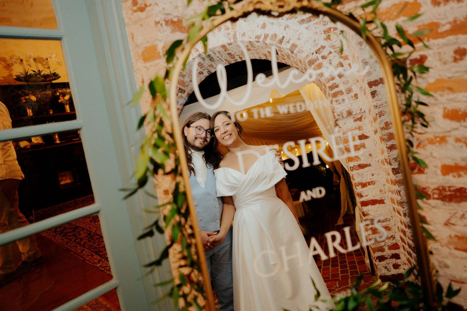 Wedding venue decorated with floral arch and signage against exposed brick wall.